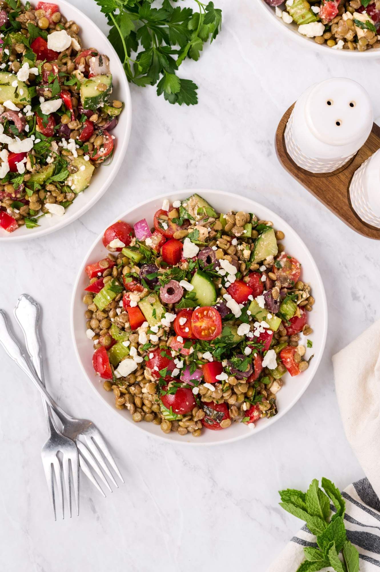 Mediterranean Lentil Salad with tomatoes, cooked lentils, cucumbers, feta cheese, and olives with vinaigrette in two bowls.