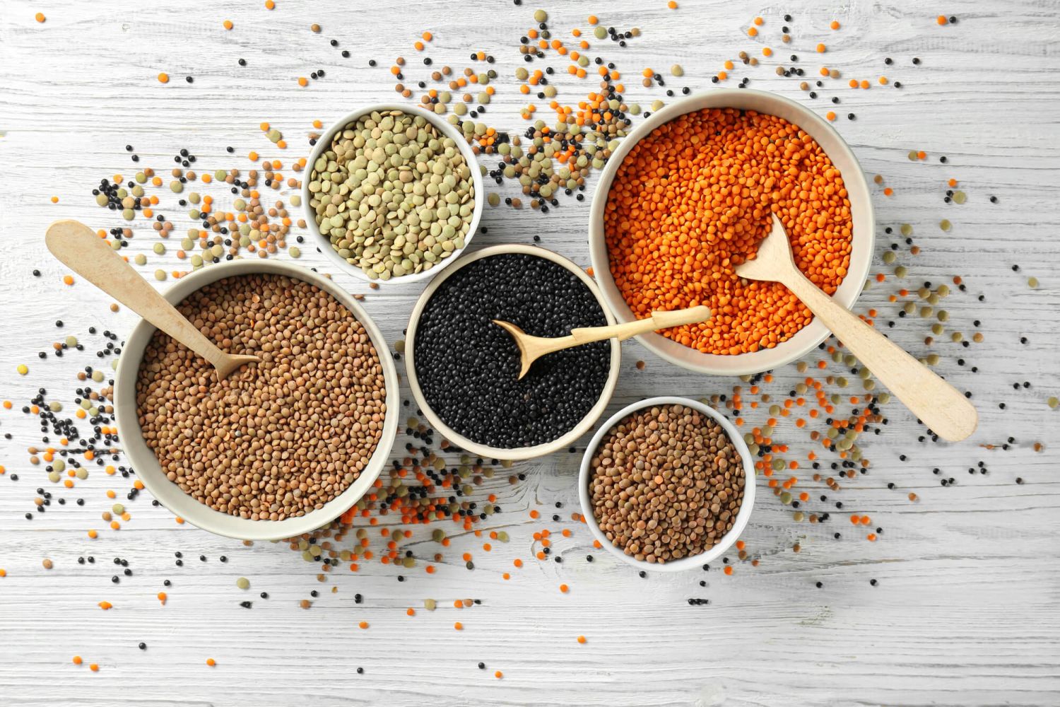 Red, brown, green, French, and black lentils in different bowls.