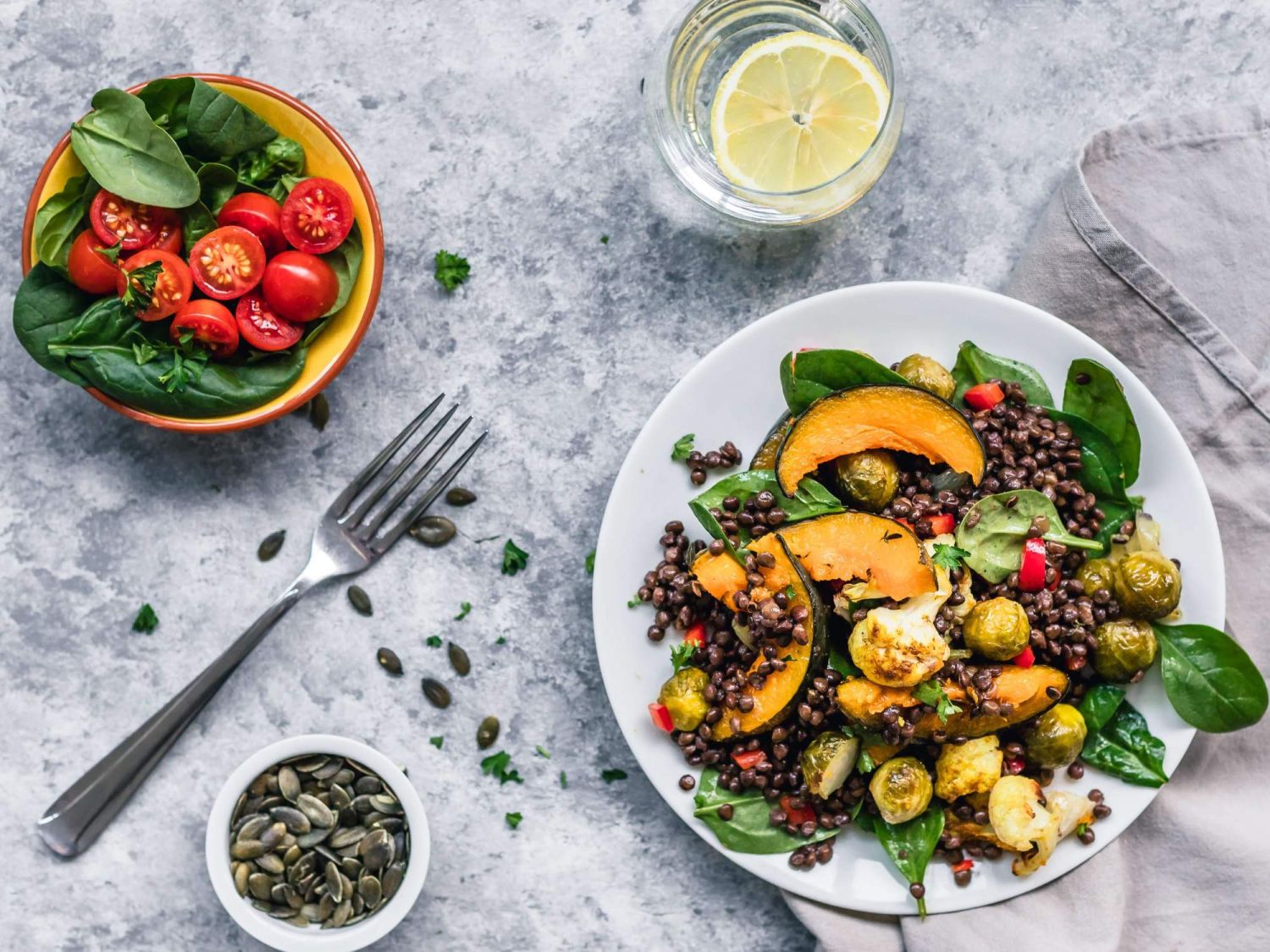 Lentil salad with spinach, Brussels sprouts, and peaches in a bowl with lemon water on the side.