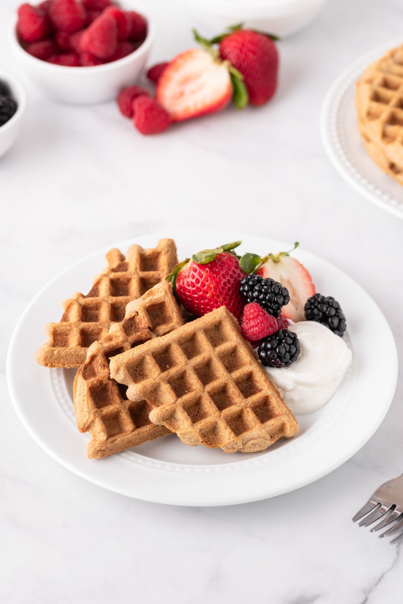 Keto waffles served on a plate with yogurt, strawberries, blackberries, and raspberries.