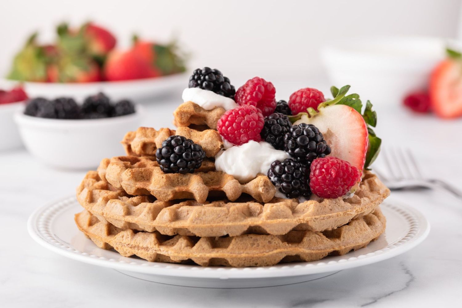 Almond flour low carb waffles stacked on a plate with fresh berries and yogurt.