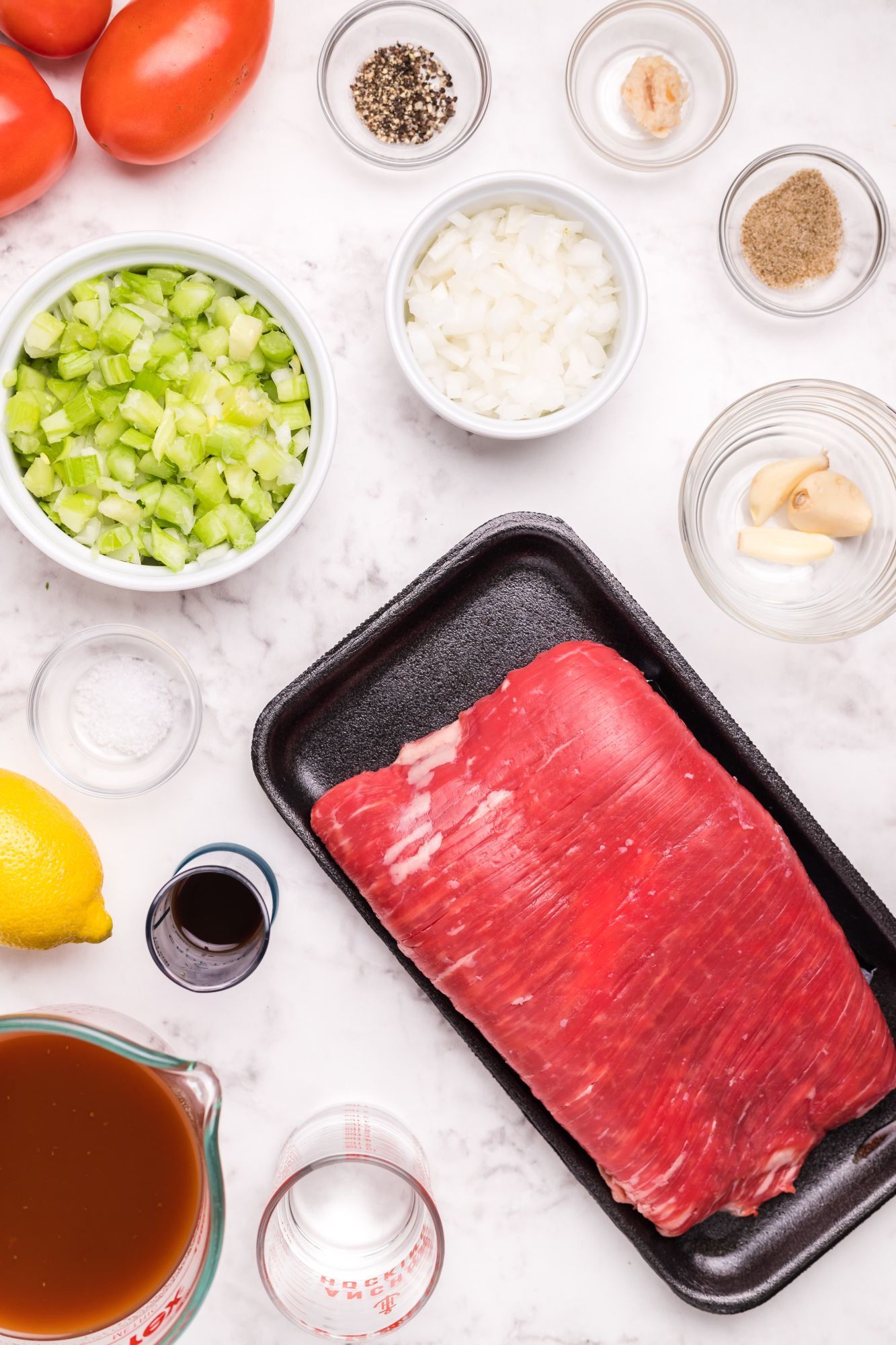 Ingredients for marinated flank steak including bloody mary mix, tomatoes, celery, onion, and garlic.