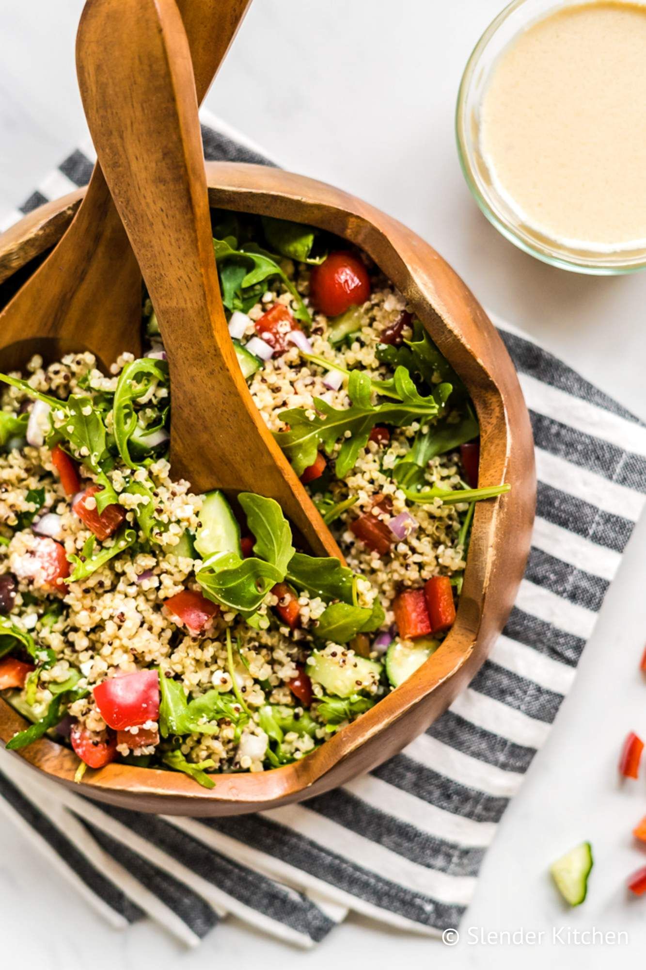 Quinoa bowl with feta cheese, olives, arugula, quinoa, and hummus dressing in a bowl with wooden utensils.