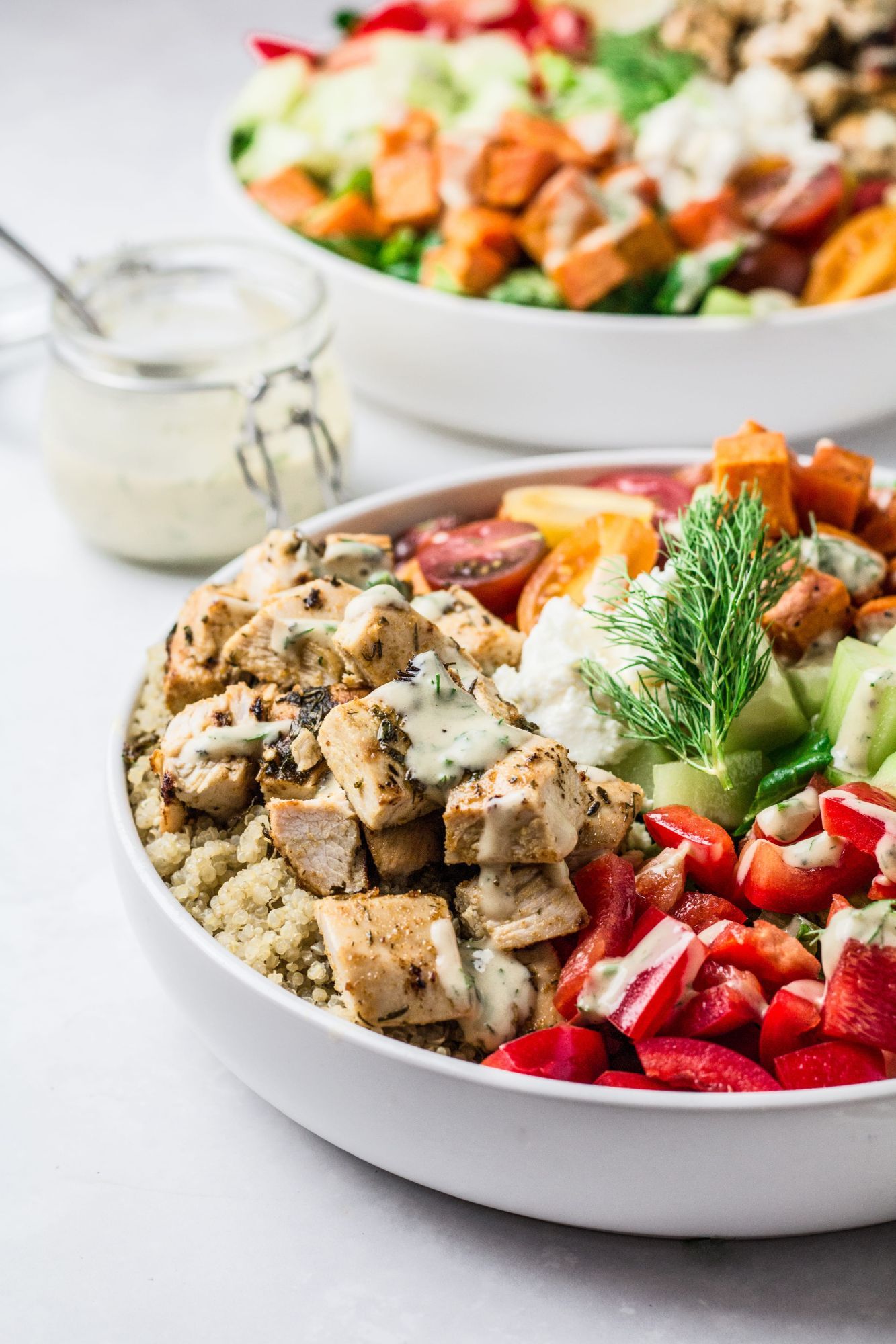 Mediterranean chicken bowls with fresh vegetables, sweet potatoes, feta cheese, and lemon slices.