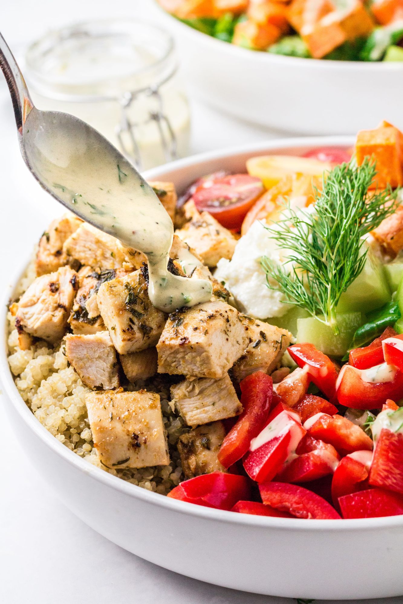 Mediterranean grain bowls with chicken, quinoa, vegetables, and a spoonful of tahini dressing.