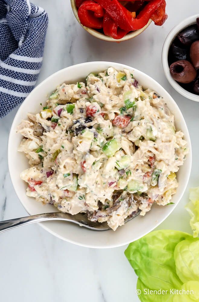 Mediterranean chicken salad in a bowl with roasted red peppers, olives, and feta cheese on the side.