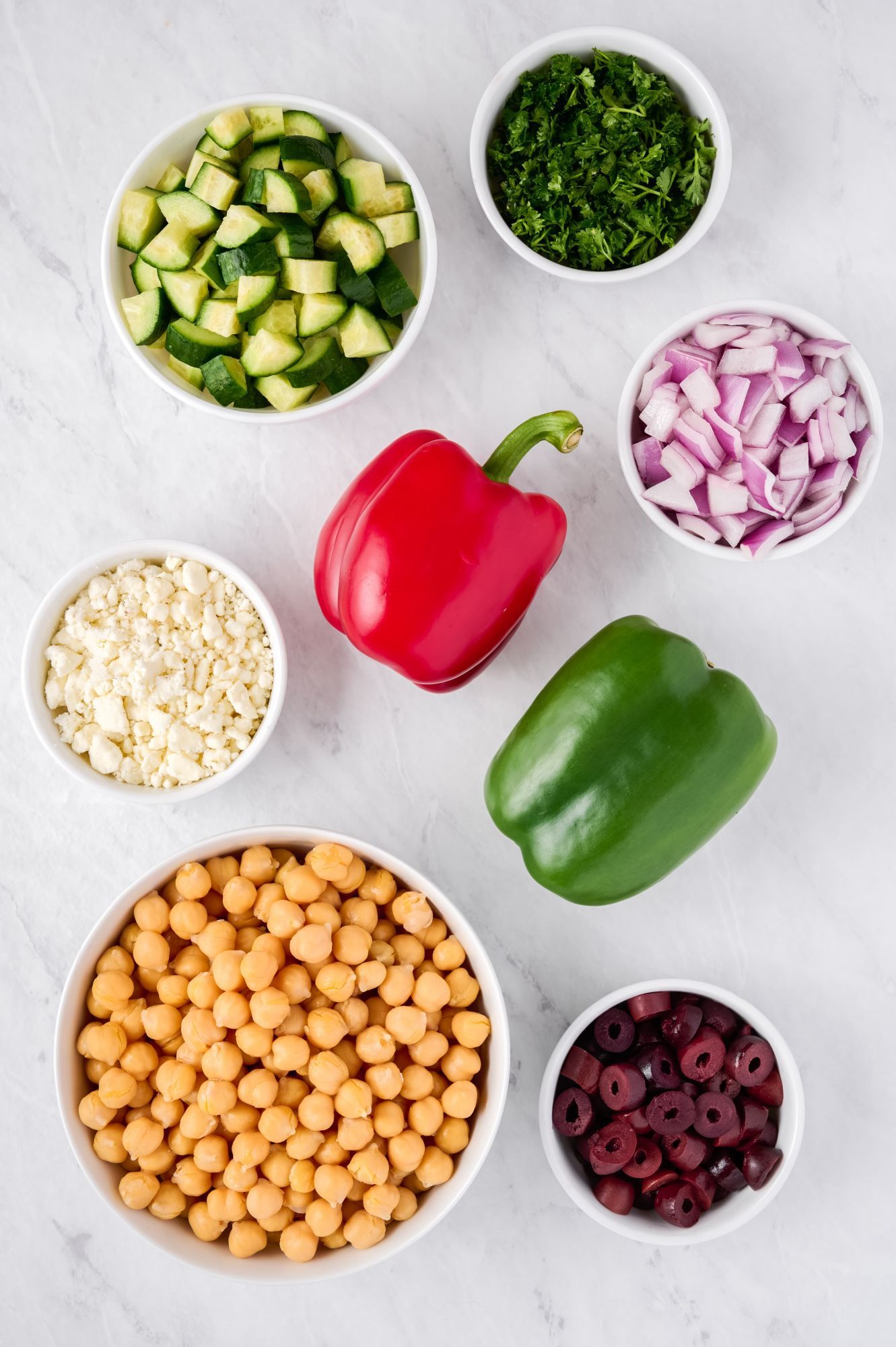 Ingredients for Mediterranean salad including chickpeas, bell peppers, kalamata olives, cucumbers, red onion, feta cheese, and parsley.