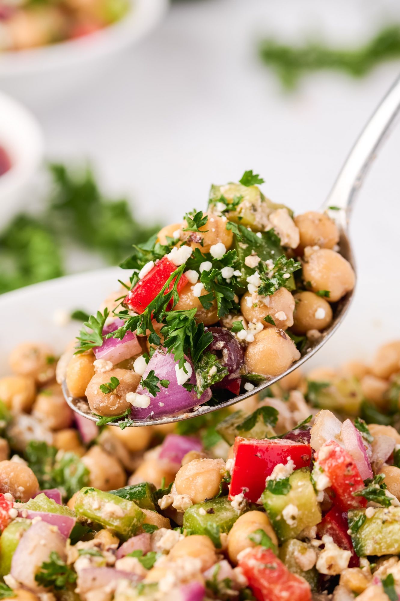 Garbanzo bean salad with feta cheese, olives, peppers, cucumbers, and red onions being picked up by a spoon.