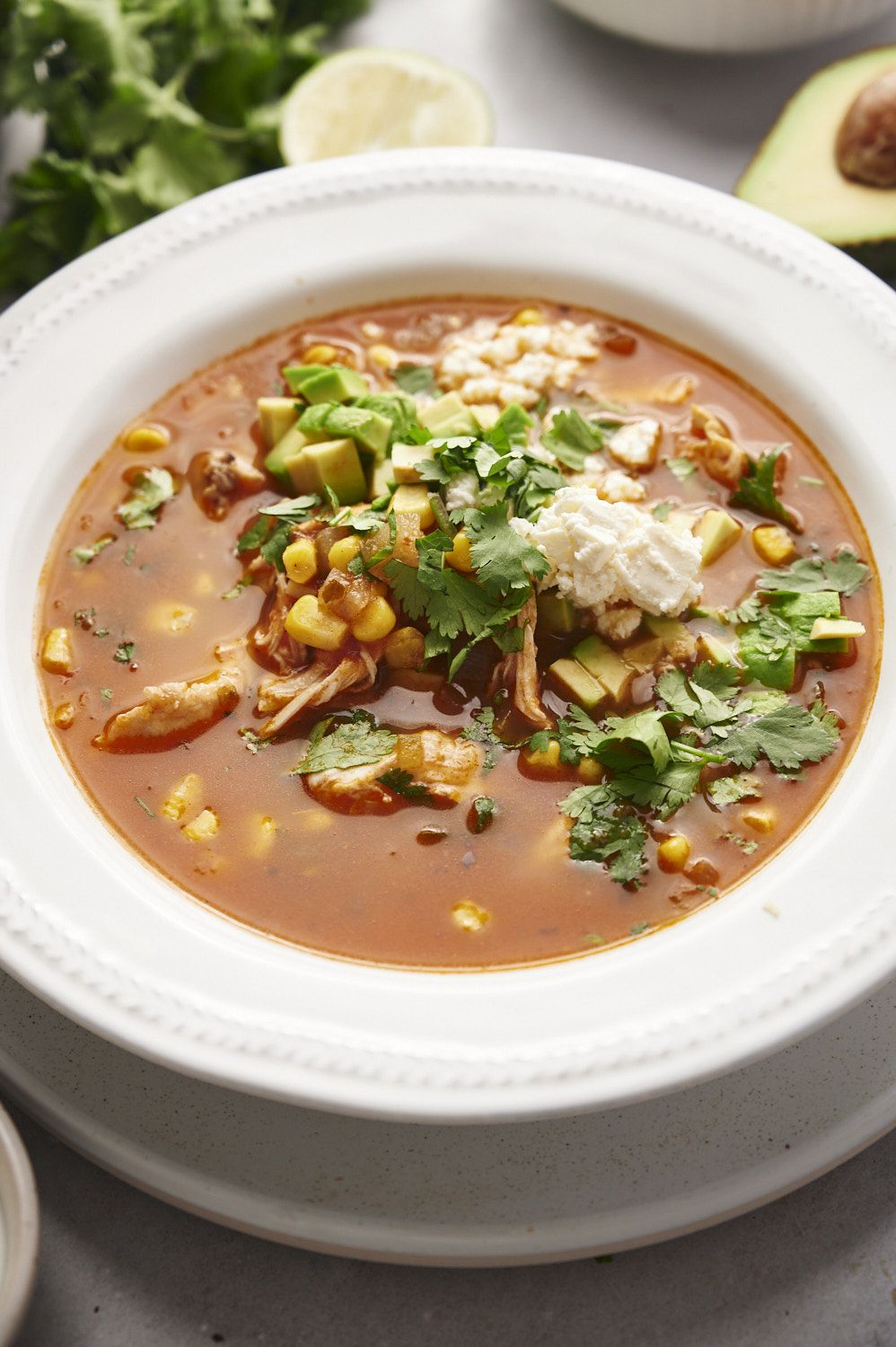 Mexican shredded chicken soup in a white bowl with queso fresco, cilantro, avocado, and corn