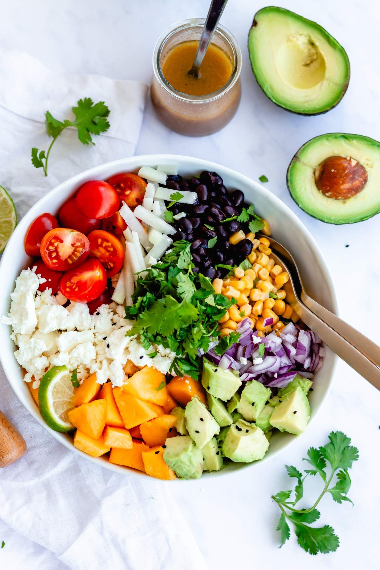 Mexican salad with avocado, black beans, tomatoes, corn, jicama, queso fresco, and a lime dressing in a bowl.