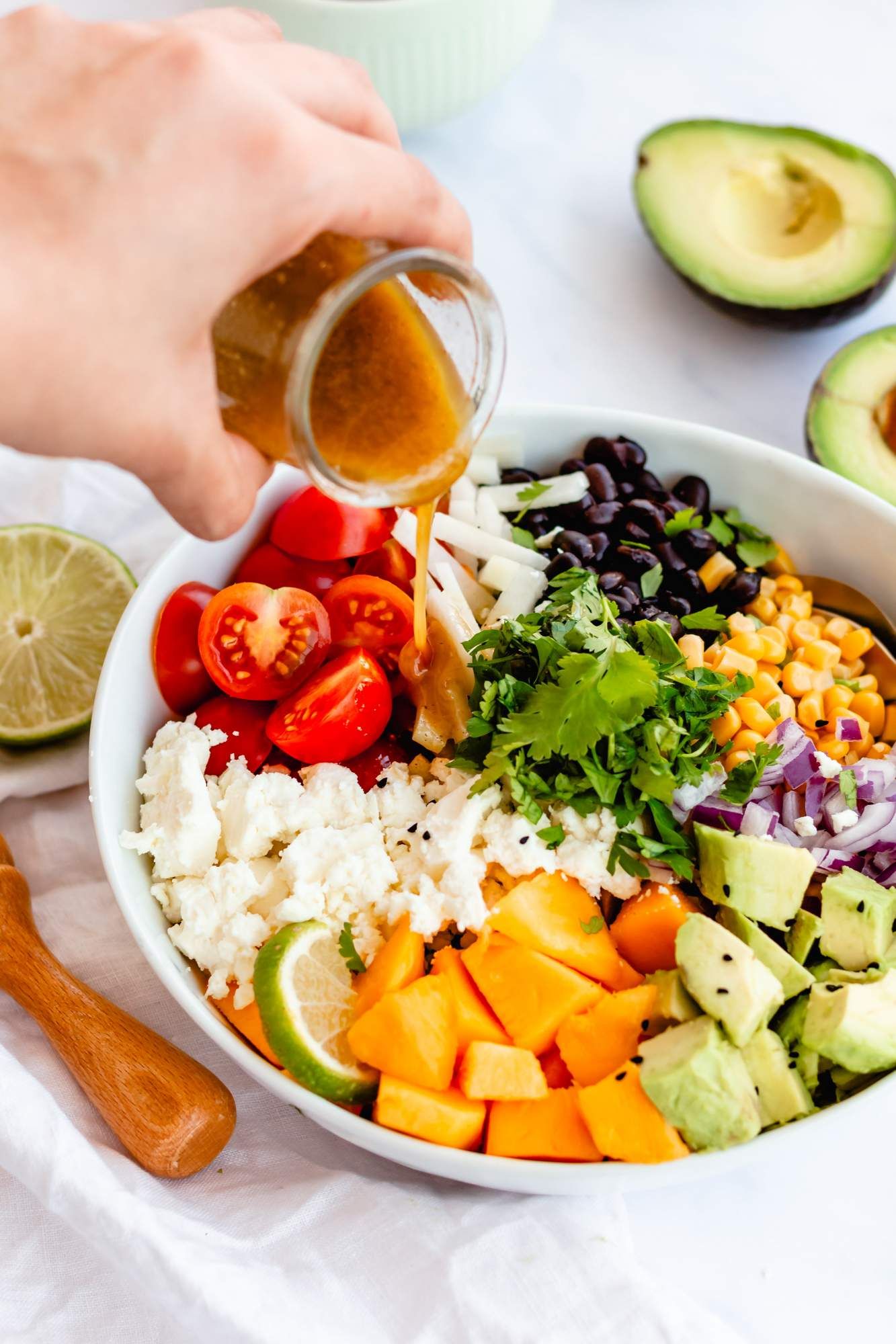 Chopped salad with Mexican ingredeints including corn, black beans, and avocado in a bowl with dressing being poured on top.