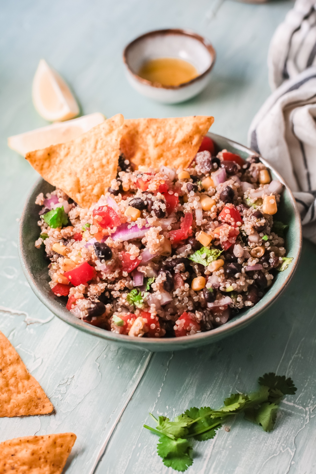 Mexican style quinoa with beans, corn, tomatoes, and cilantro in a bowl with avocado and chips.