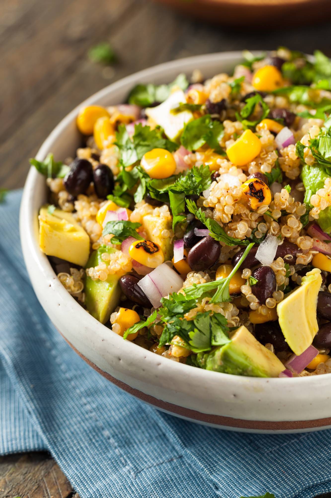 Mexican inspired quinoa salad with black beans, corn, avocado, and red onions in a bowl with cilantro.