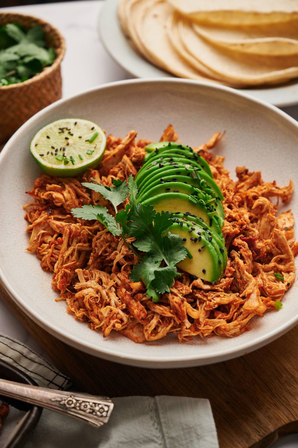 Shredded chicken in Mexican spices, tomatoes, and chipotle peppers served with slice avocado and lime in a bowl.