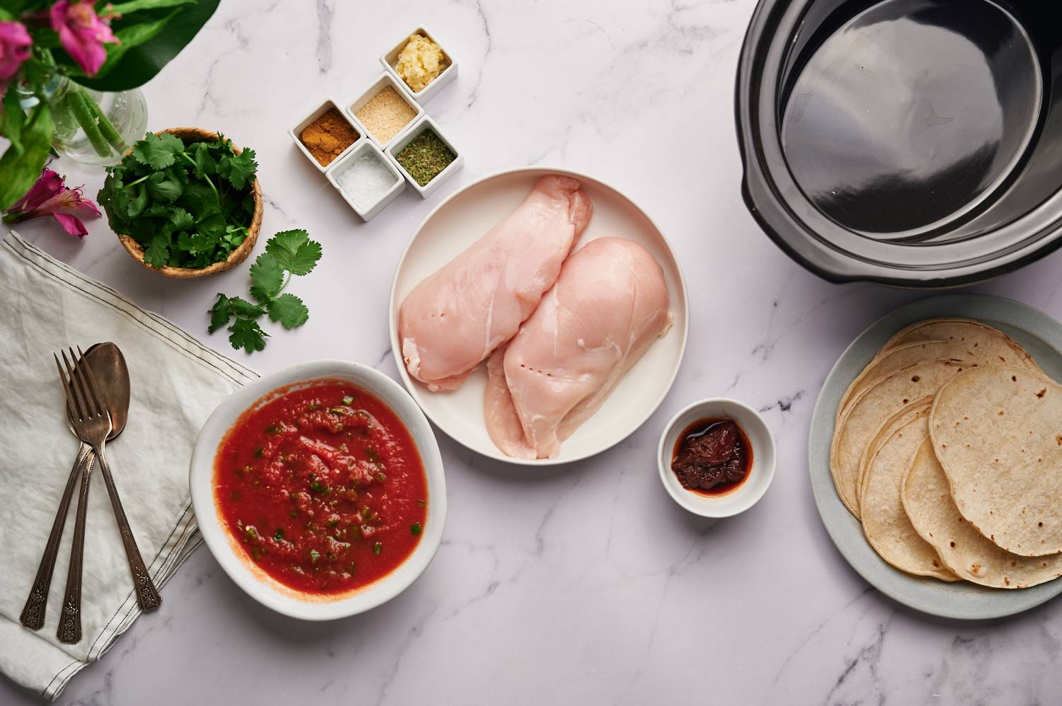 Ingredients for Mexican shredded chicken including chicken breasts, diced tomatoes, spices, cilantro, garlic, and chipotle peppers.