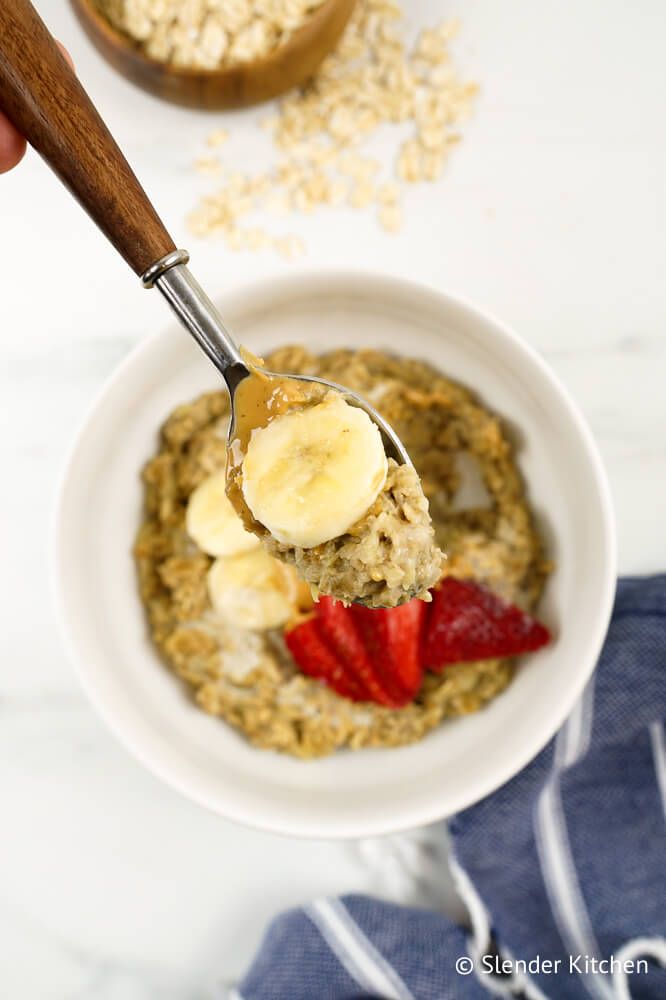 Microwave oatmeal with bananas and peanut butter on a wooden spoon with sliced banana.