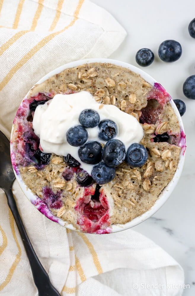 Microwave blueberry oatmeal muffin with fresh blueberries and oats in a dish with a napkin.