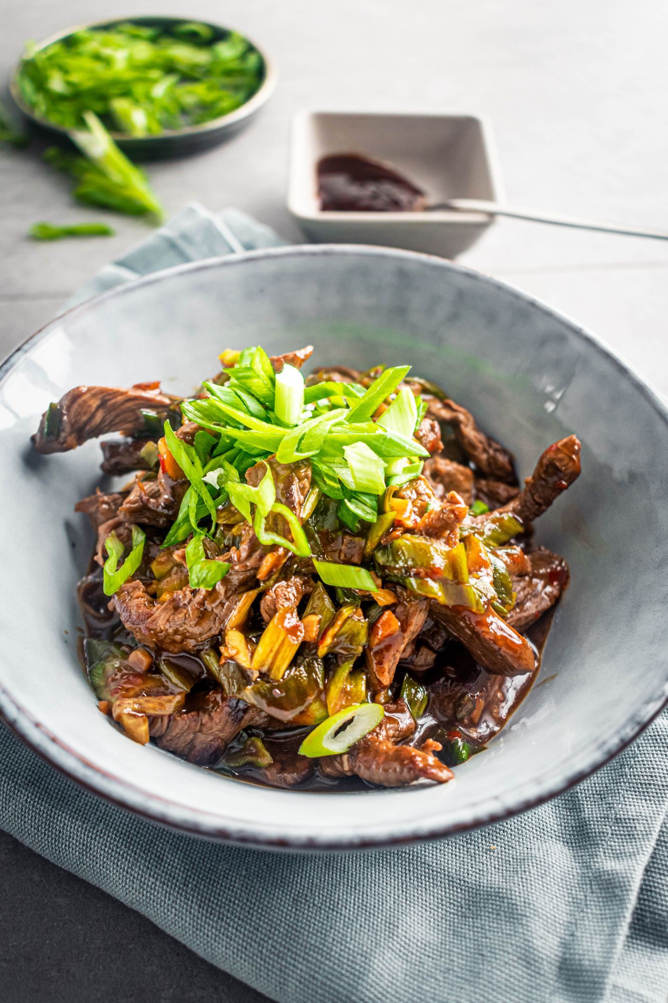 Mongolian beef stir fry with sliced green onions in a bowl with hoisin sauce on the side.