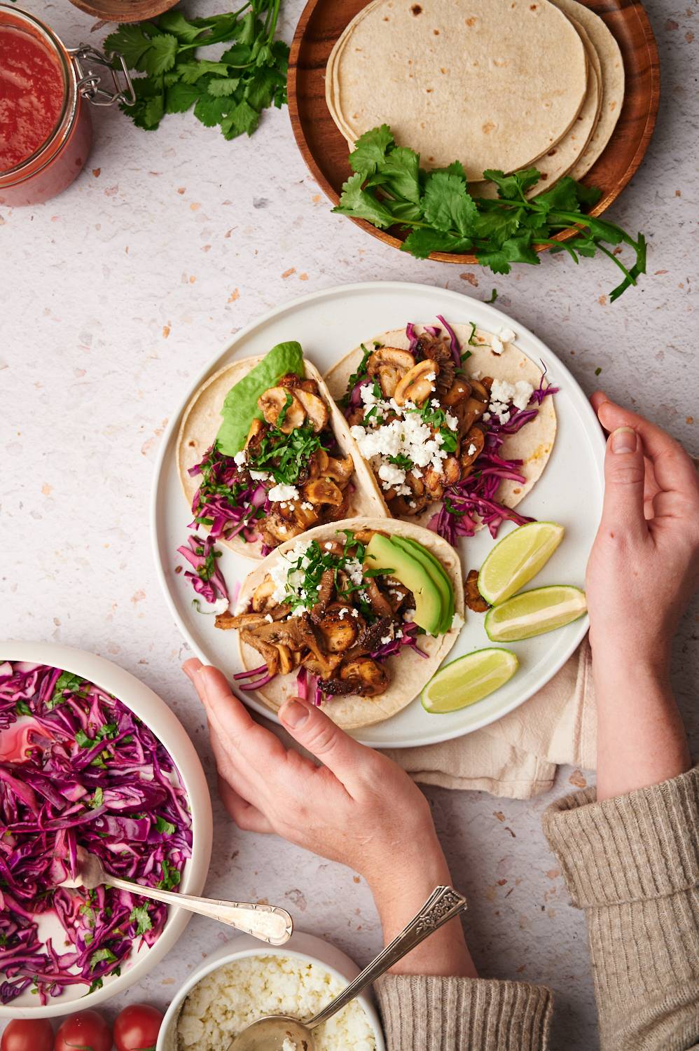 Tacos with mushrooms served with red cabbage, cilantro, queso fresco, avocado, and limes on a plate.