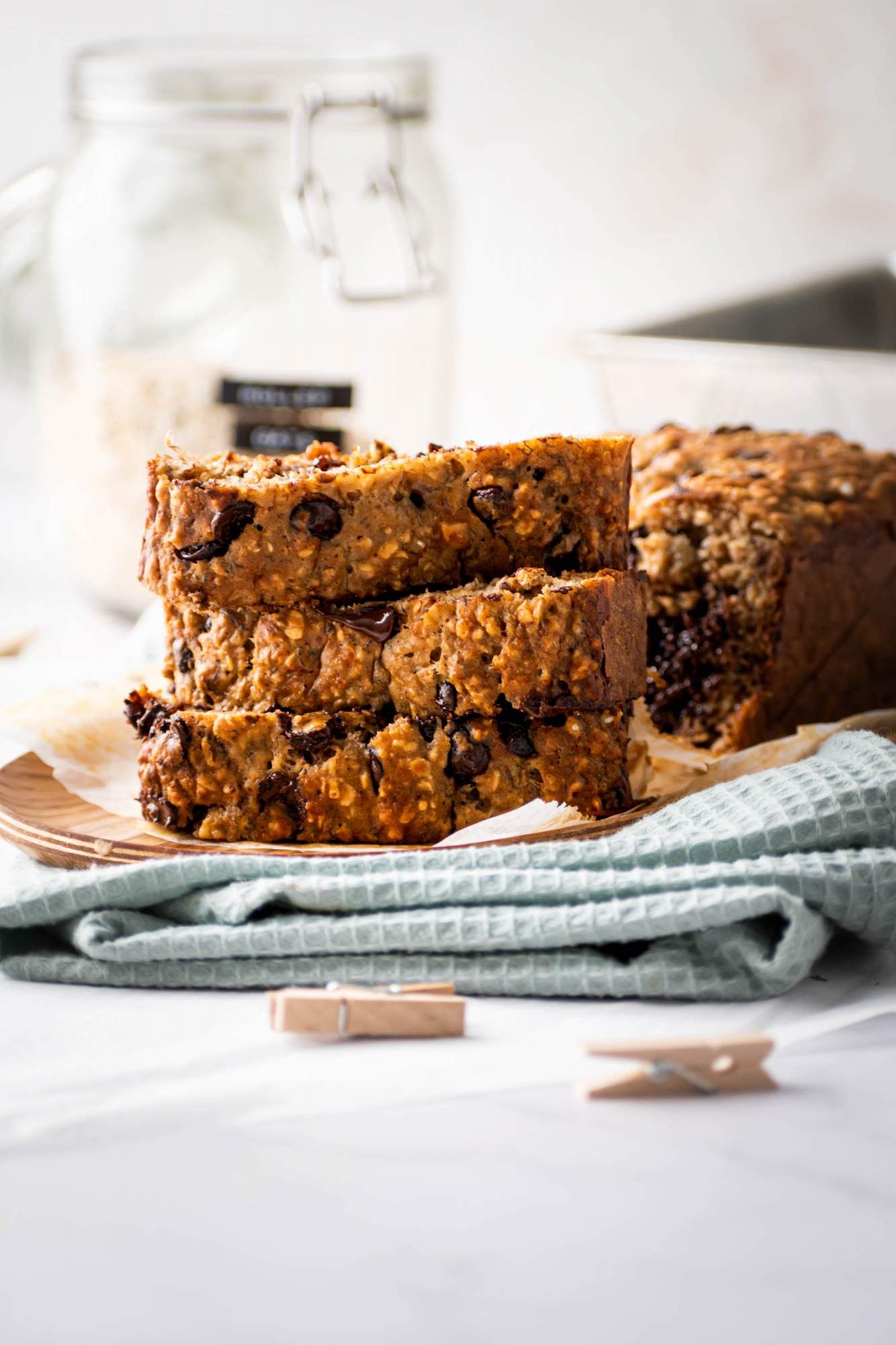 Slices of banana oatmeal bread with chocolate chips stacked up with oats in the background.