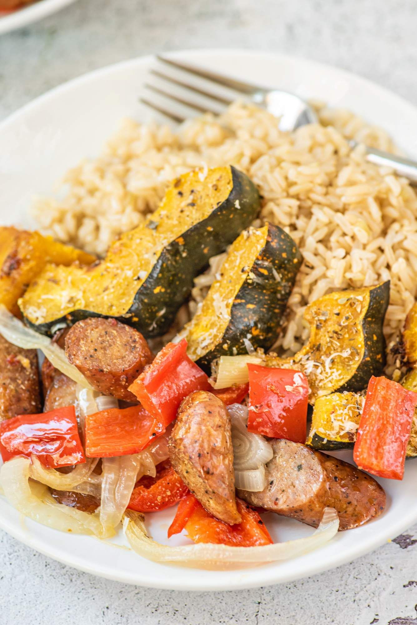 Sausage with acorn squash, onions, and bell peppers on a plate with brown rice.