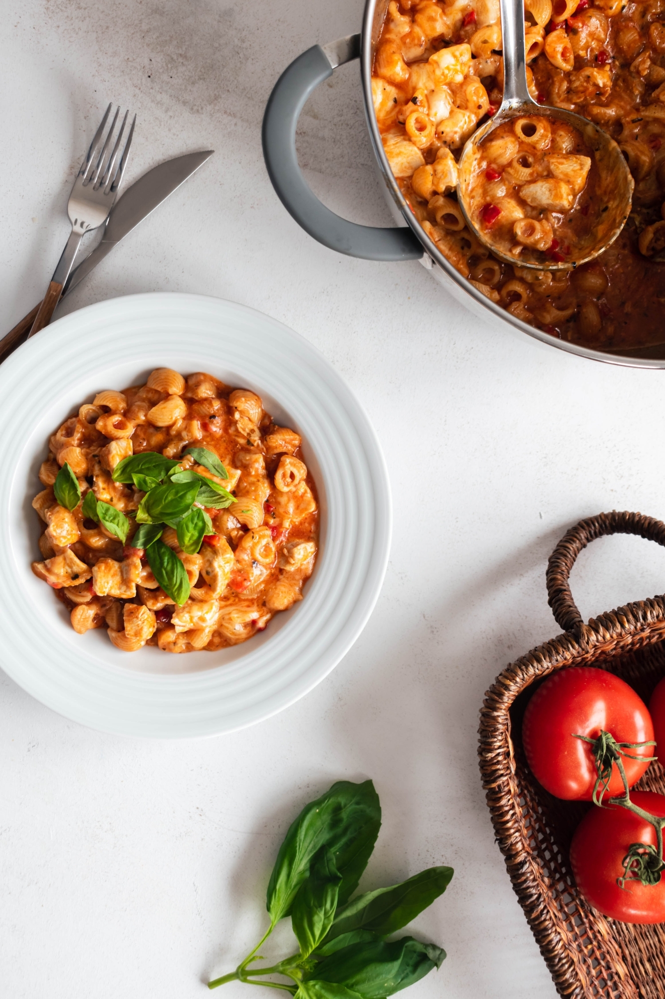 One pot pasta with chicken breast, marinara sauce, cheese, and basil in a bowl and in a pot.