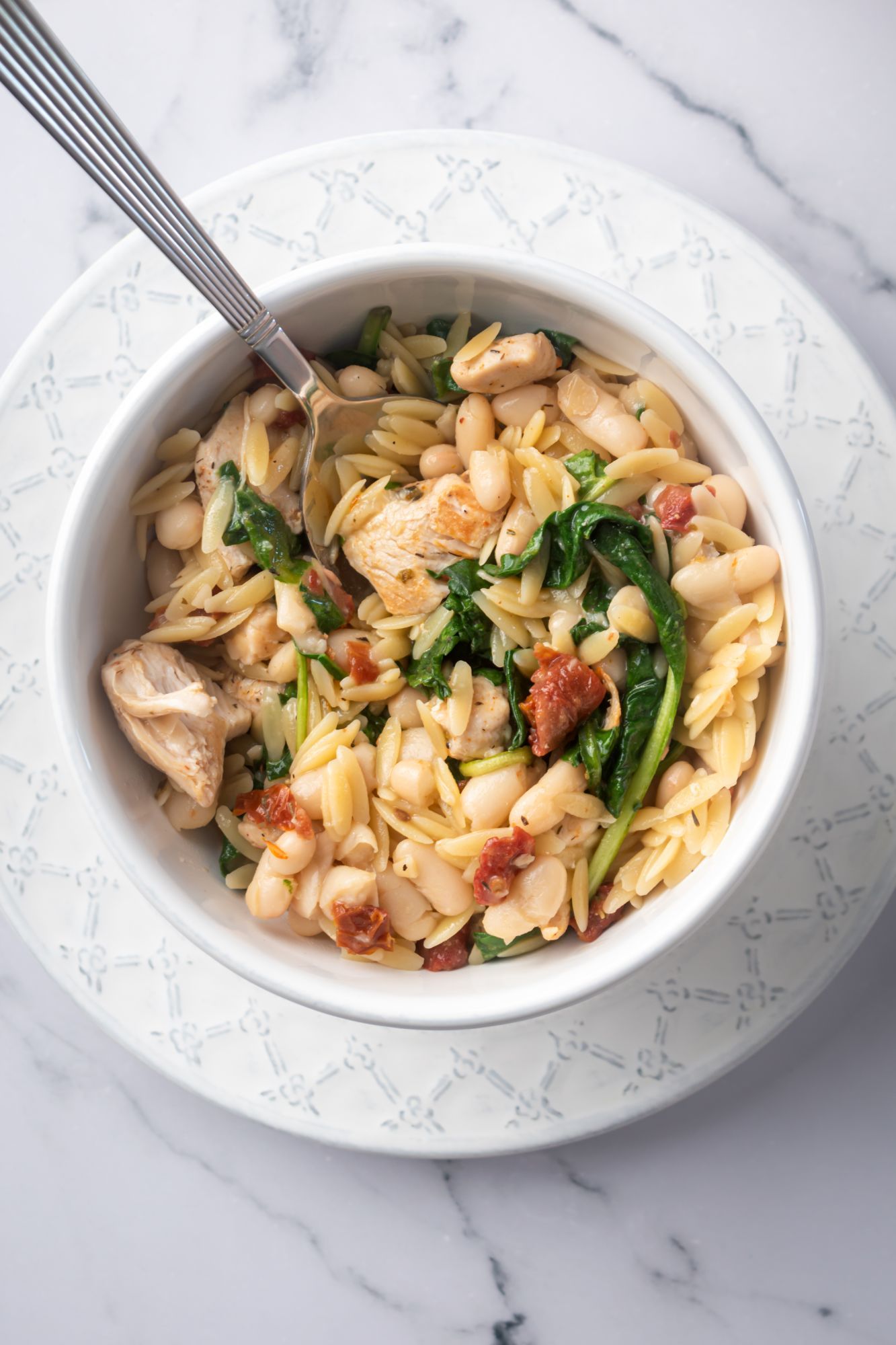 Orzo with chicken breast, spinach, white beans, and sundried tomatoes in a bowl with a spoon.