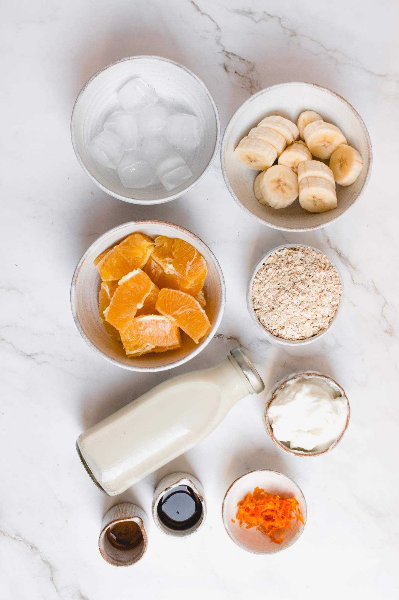 Ingredients to make a creamsicle smoothie including oranges, bananas, oats, almond milk, and vanilla extract.