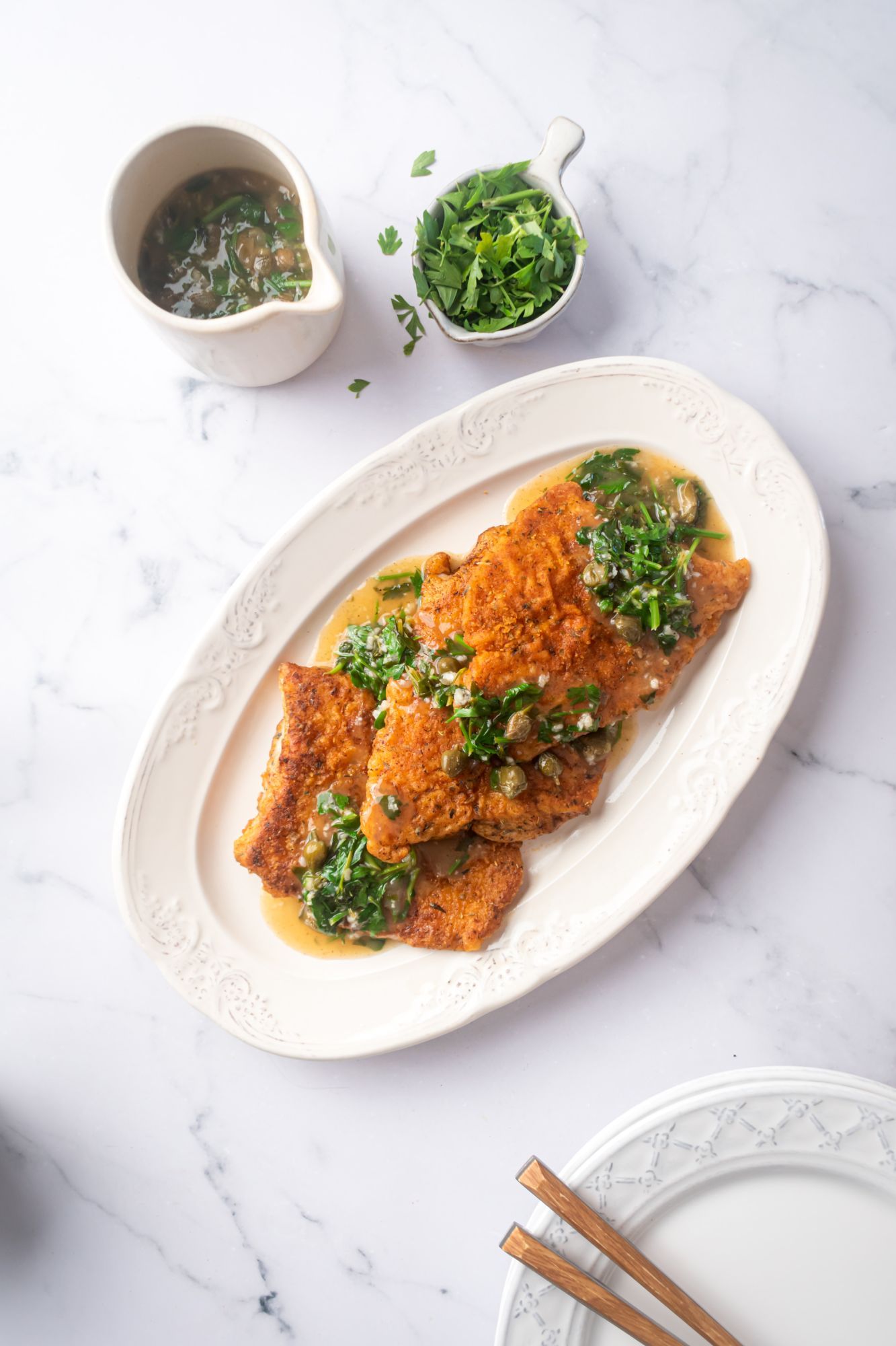 Seared cod with a crispy exterior served on a plate with lemon, capers, and parsley.