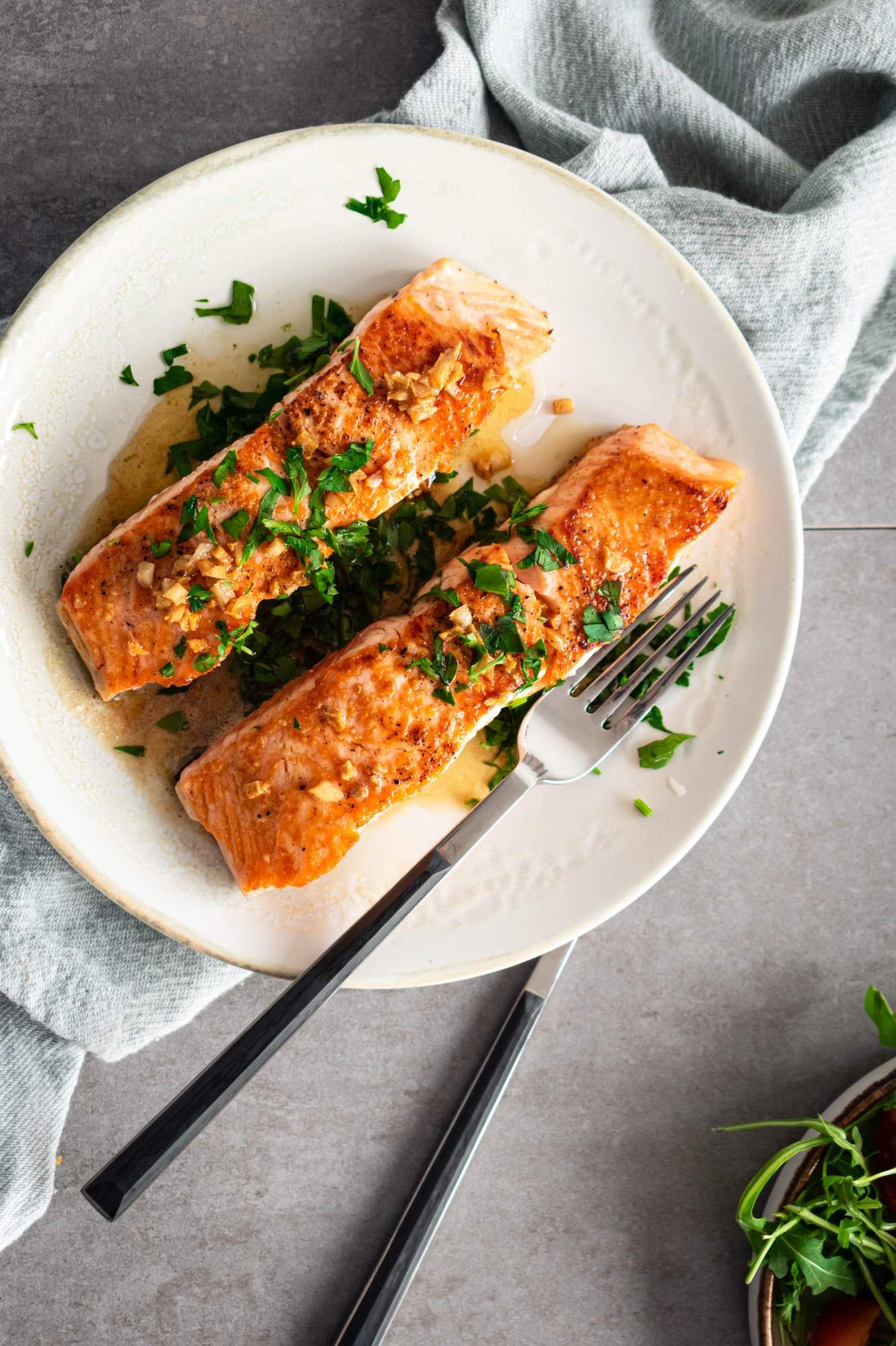 Garlic butter pan seared salmon with a crispy exterior on a plate with salad on the side.