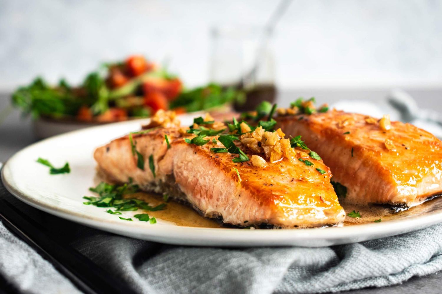 Pan fried salmon with garlic, butter, and lemon sauce on a plate with parsley.