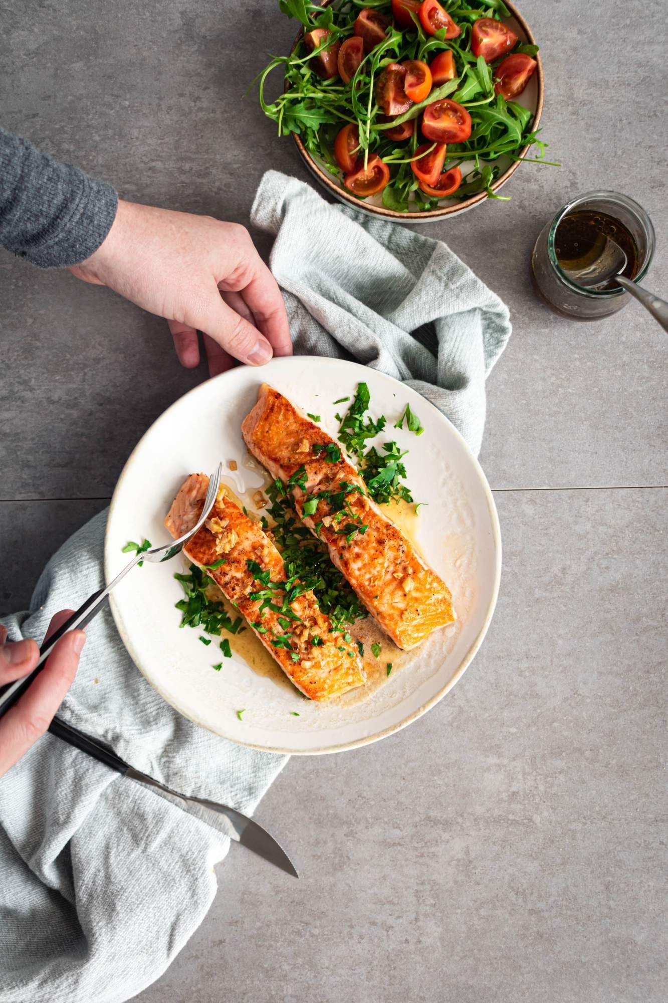 Seared salmon with a lemon, garlic, and butter sauce on a plate with a green salad on the side.