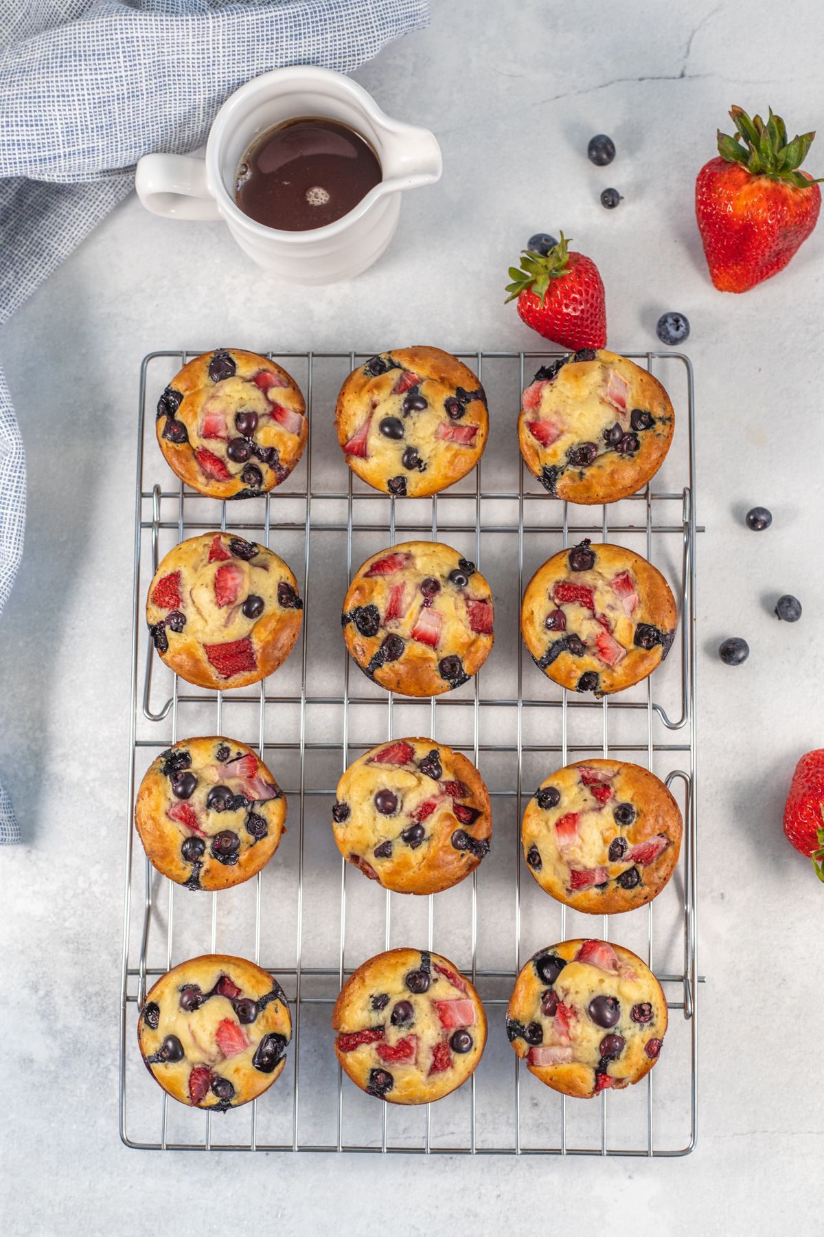 Muffins made with pancake batter with strawberries and blueberries on a wire rack.