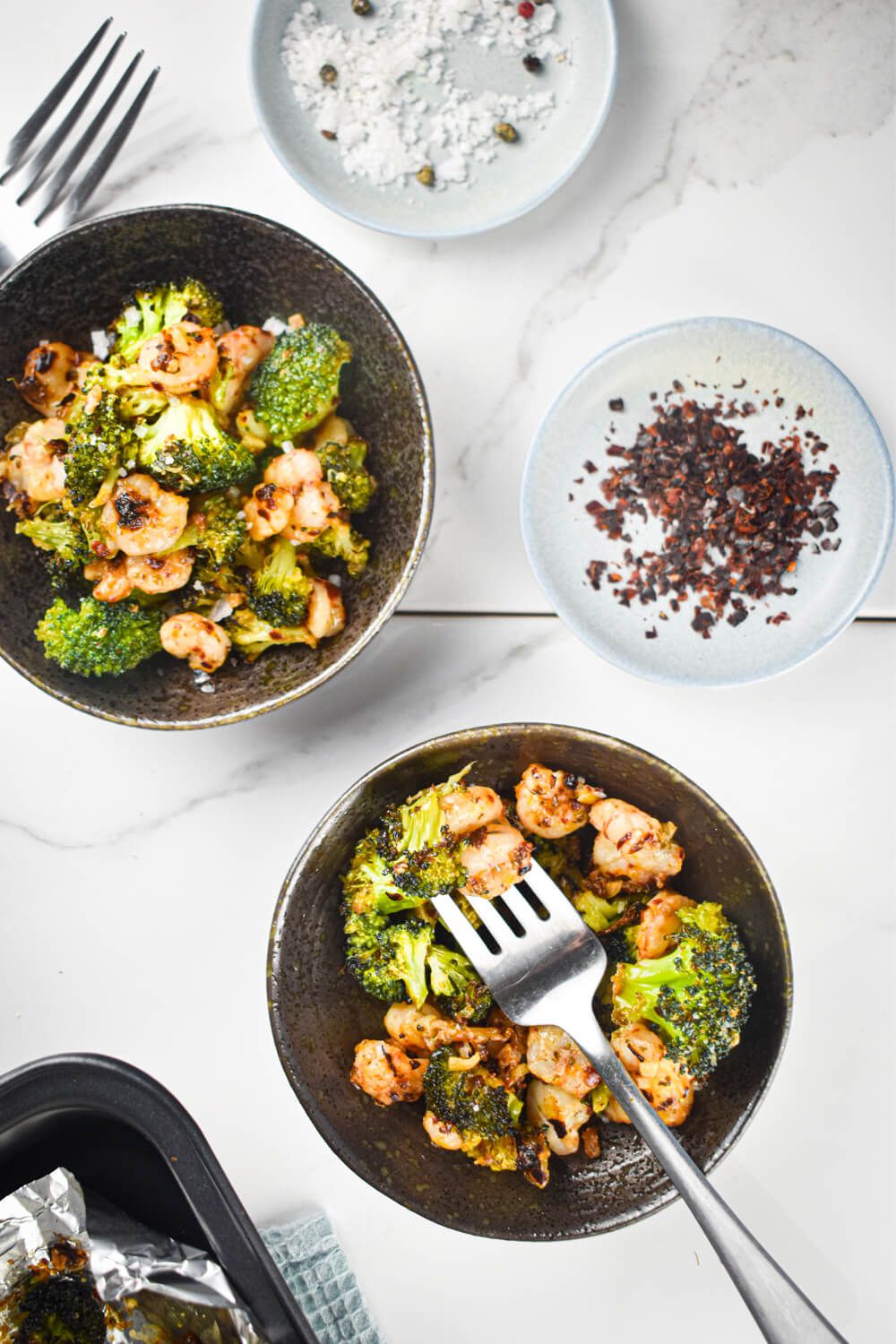 Garlic Shrimp and Broccoli on two plates with red pepper flakes, garlic, lemon, and salt.