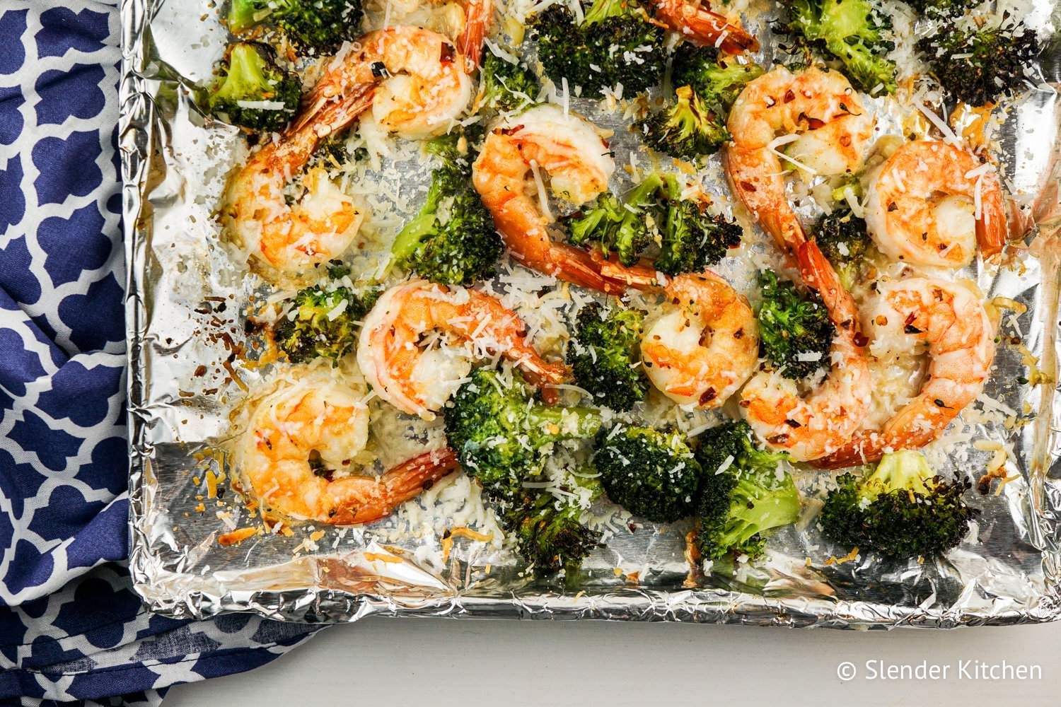 Roasted shrimp and brocolli on a sheet pan covered with foil and topped with Parmesan chese.