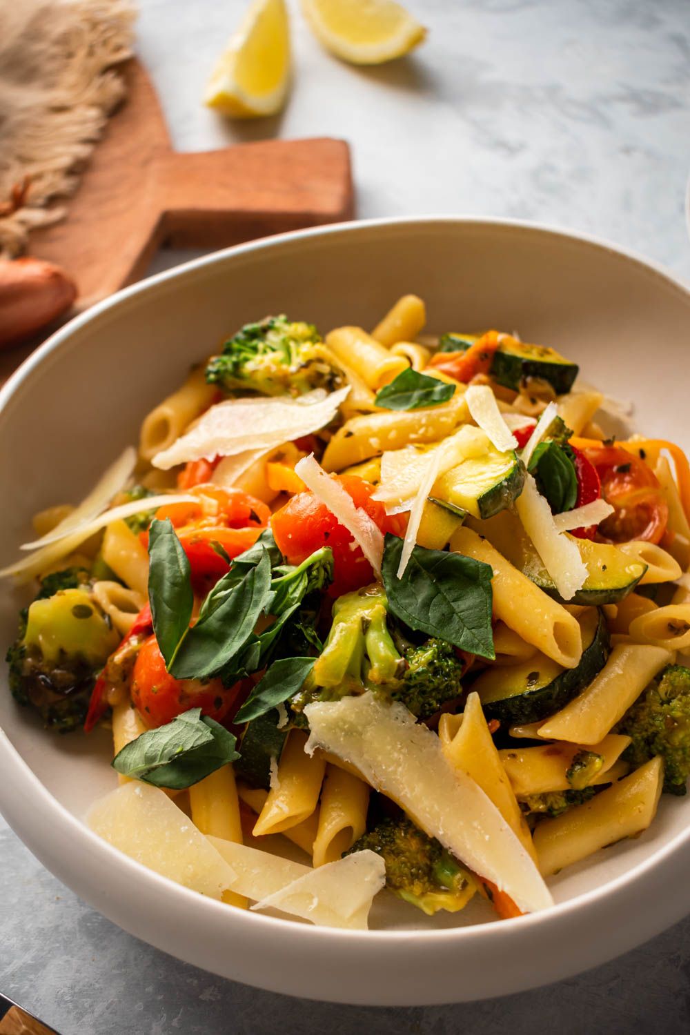 Fresh penne pasta primavera with broccoli, zucchini, carrots, and tomatoes in a bowl with Parmesan cheese.