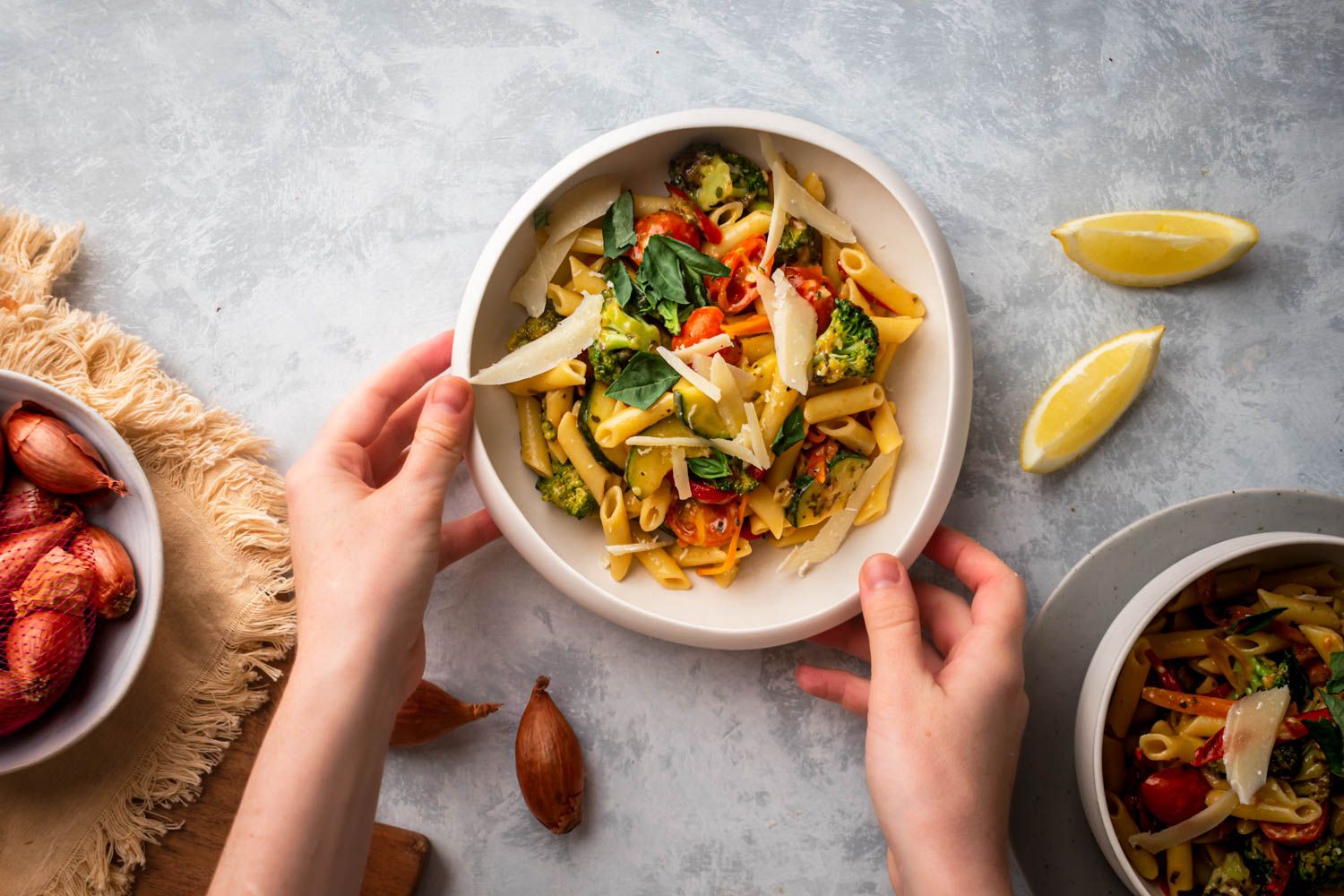 Primavera pasta with fresh tomatoes, broccoli, carrots, and zucchini in a bowl with Parmesan, basil, and lemon.