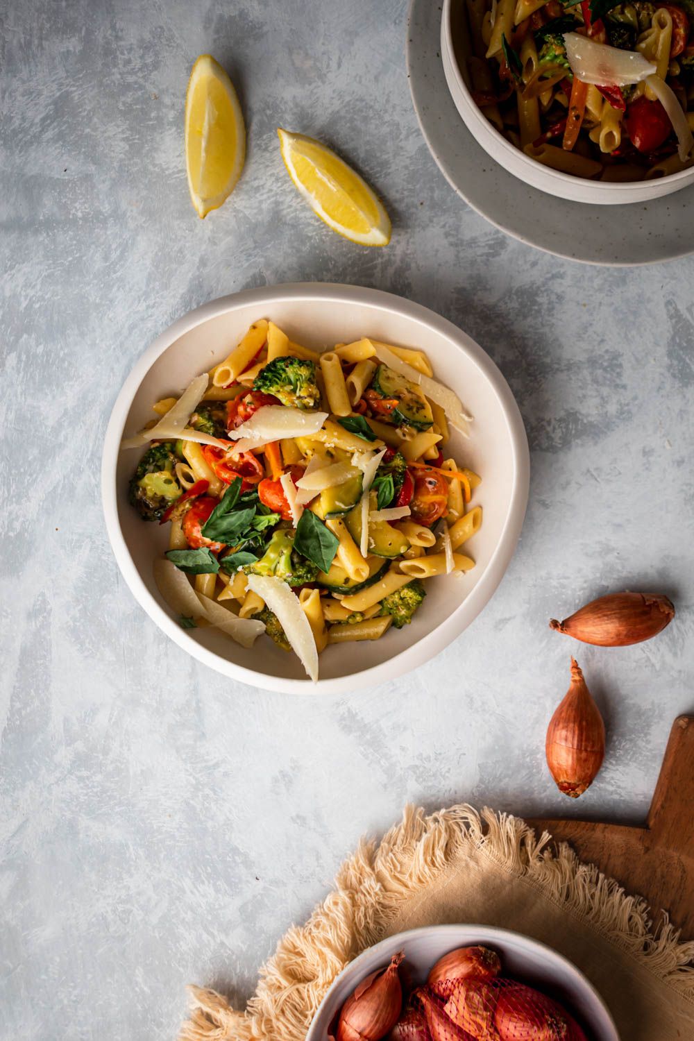 Fresh vegetable primavera with penne pasta in a bowl with sliced lemon and basil.