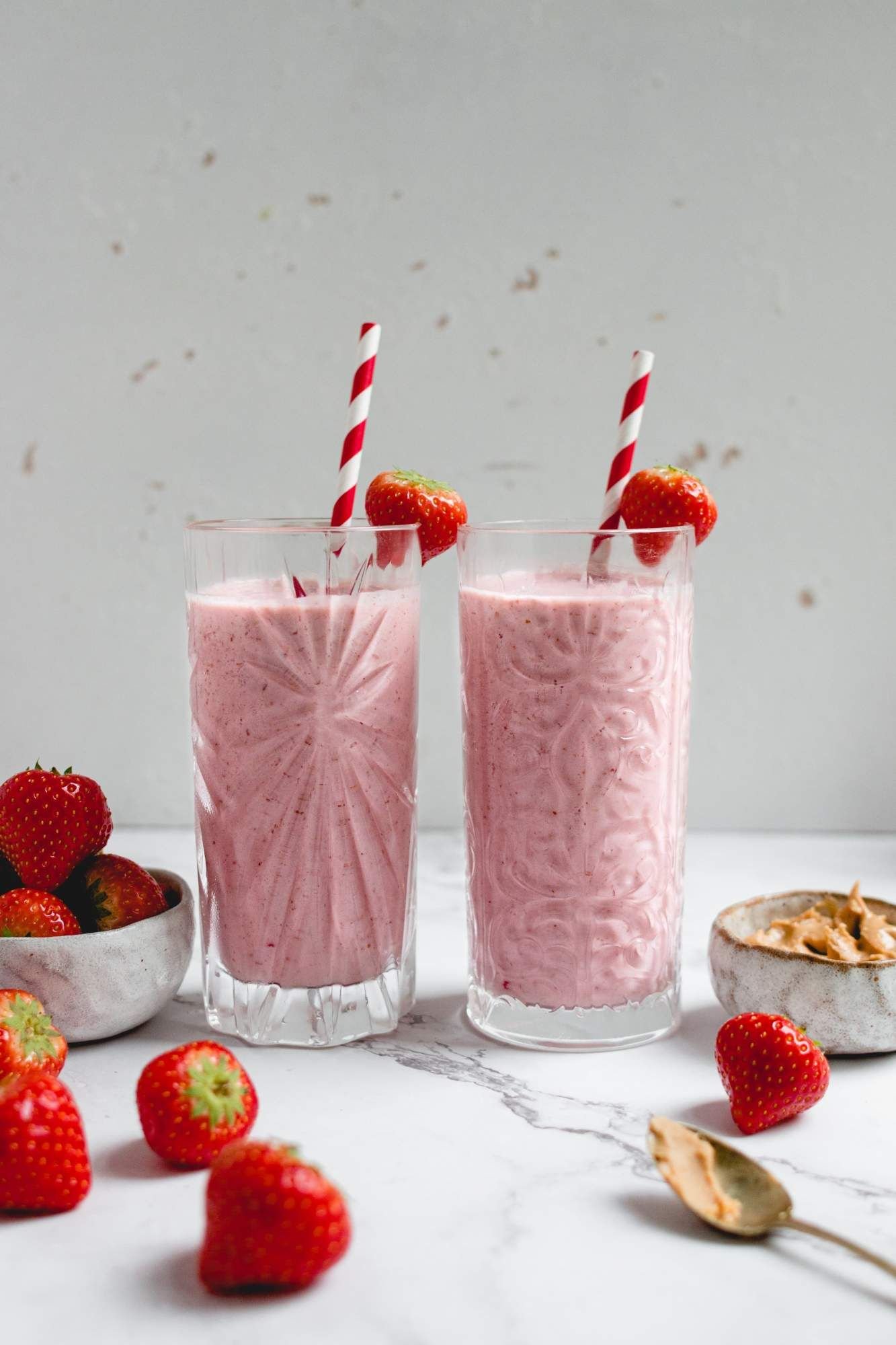 Peanut butter and jelly smoothie in two glasses with strawberries on the side.