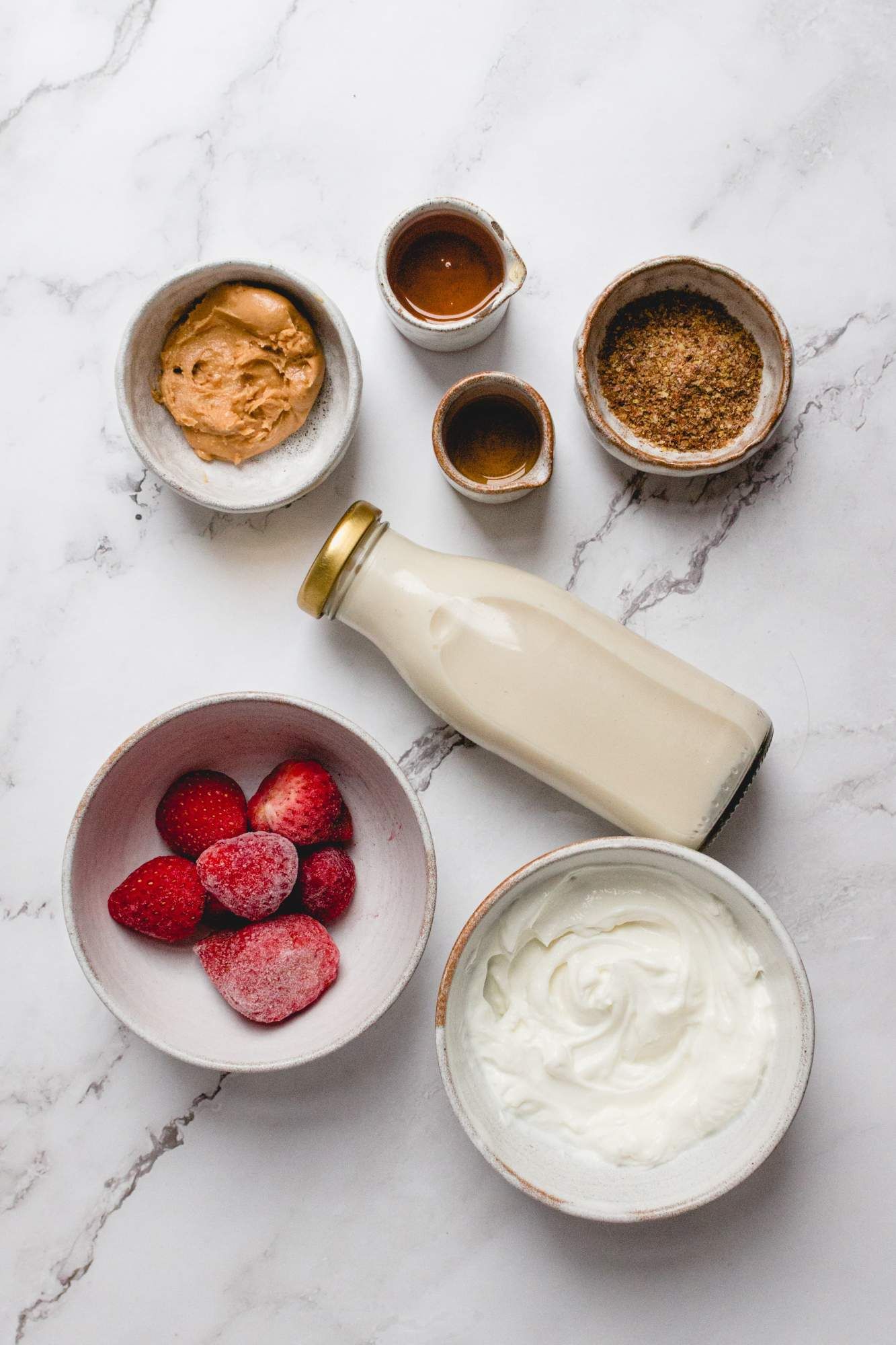 Ingredients for a peanut butter and jelly smoothie including strawberries, peanut butter, almond milk, yogurt, and flaxseeds.