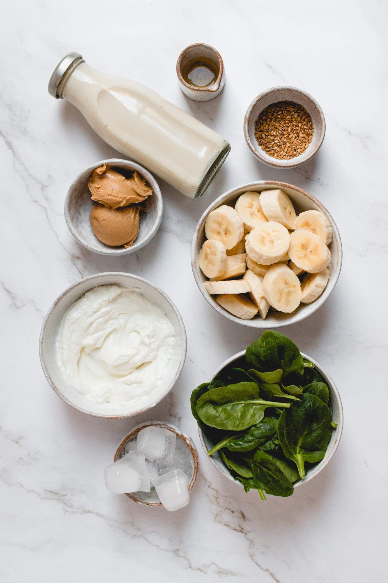 Ingredients for a banana green smoothie with peanut butter, yogurt, spinach, and almond milk.