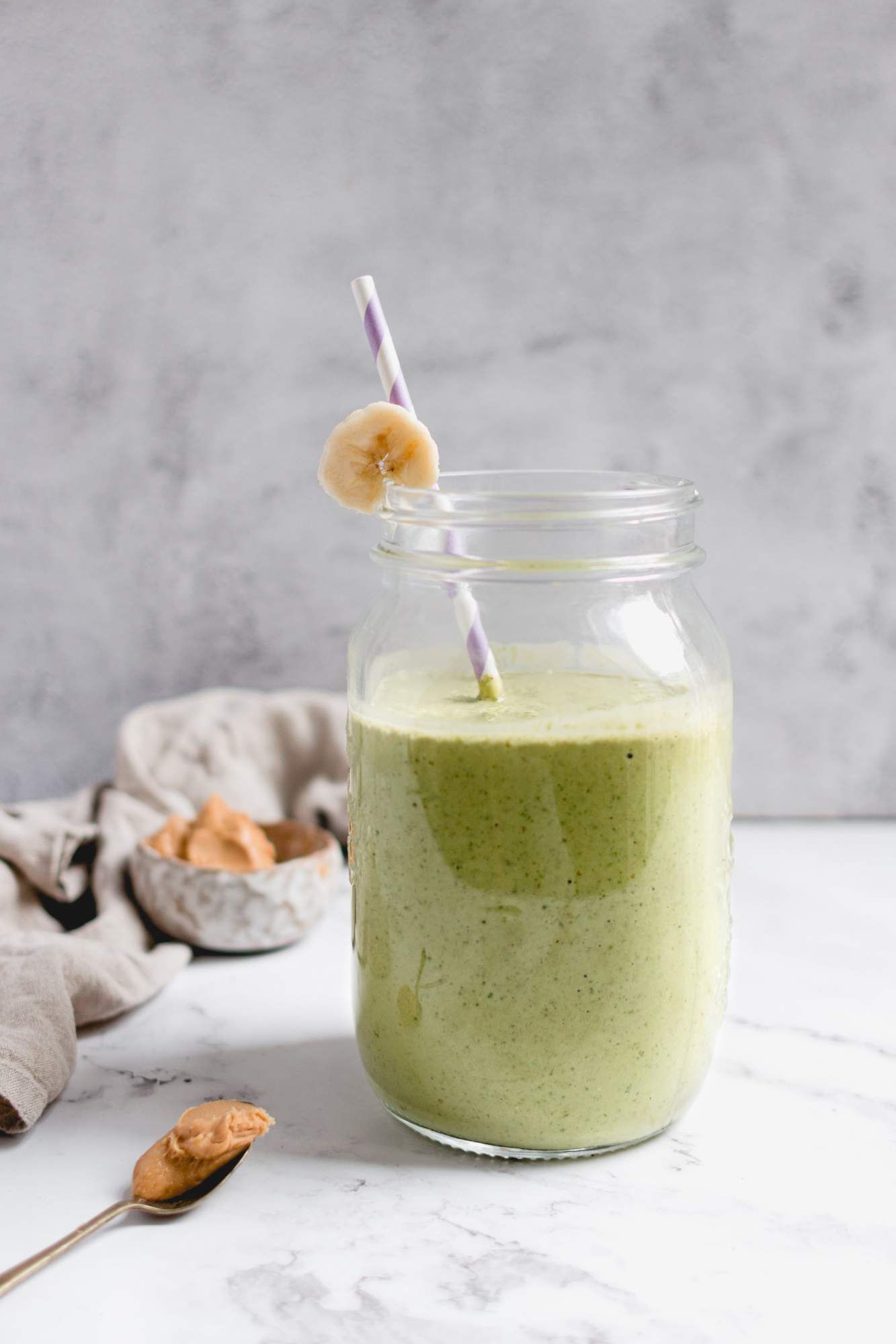 Green smoothie with banana and peanut butter in a glass with peanut butter on the side.