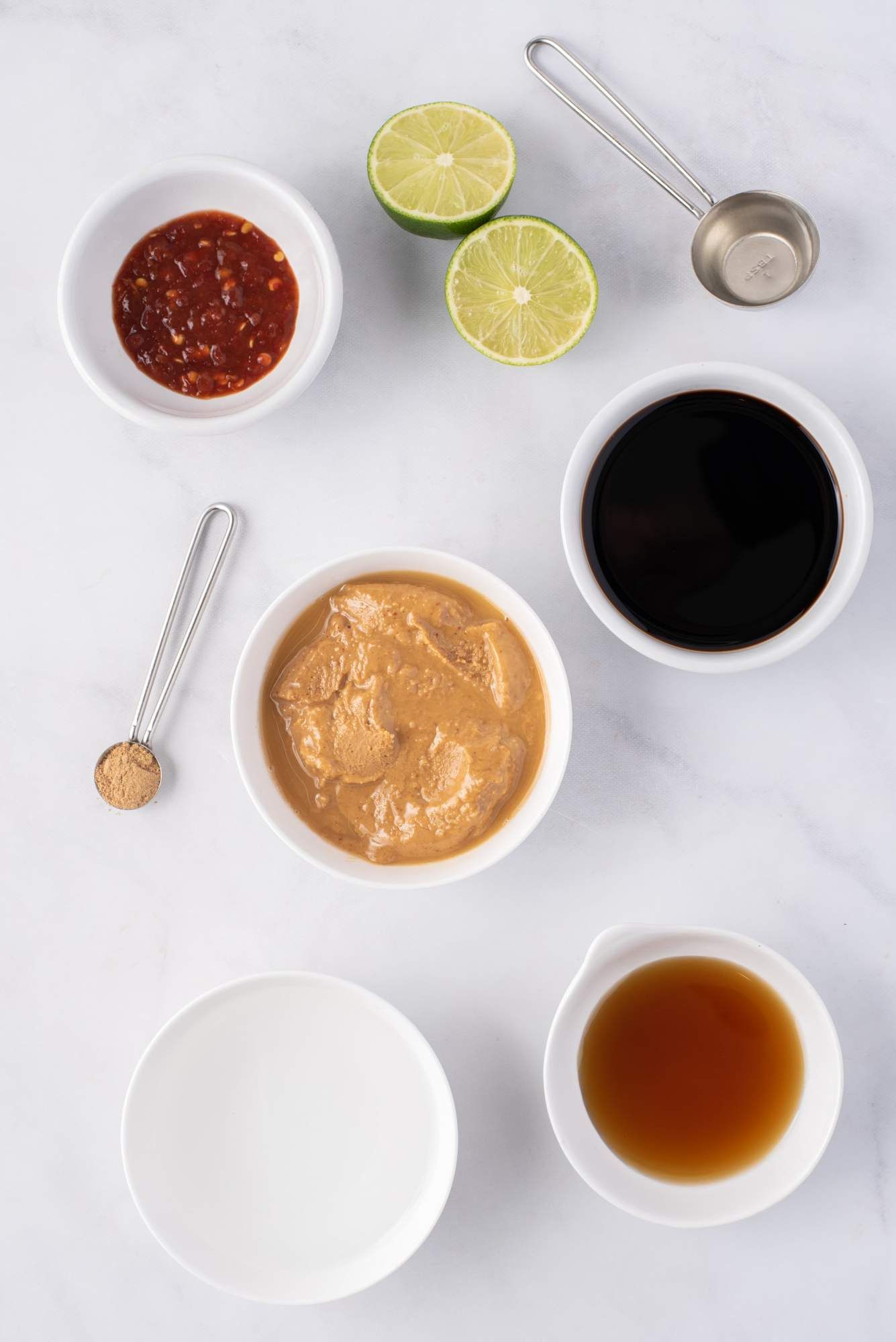 Ingredients for peanut sauce including peanut butter, limes, soy sauce, ground ginger, maple syrup, and Asian hot sauce,