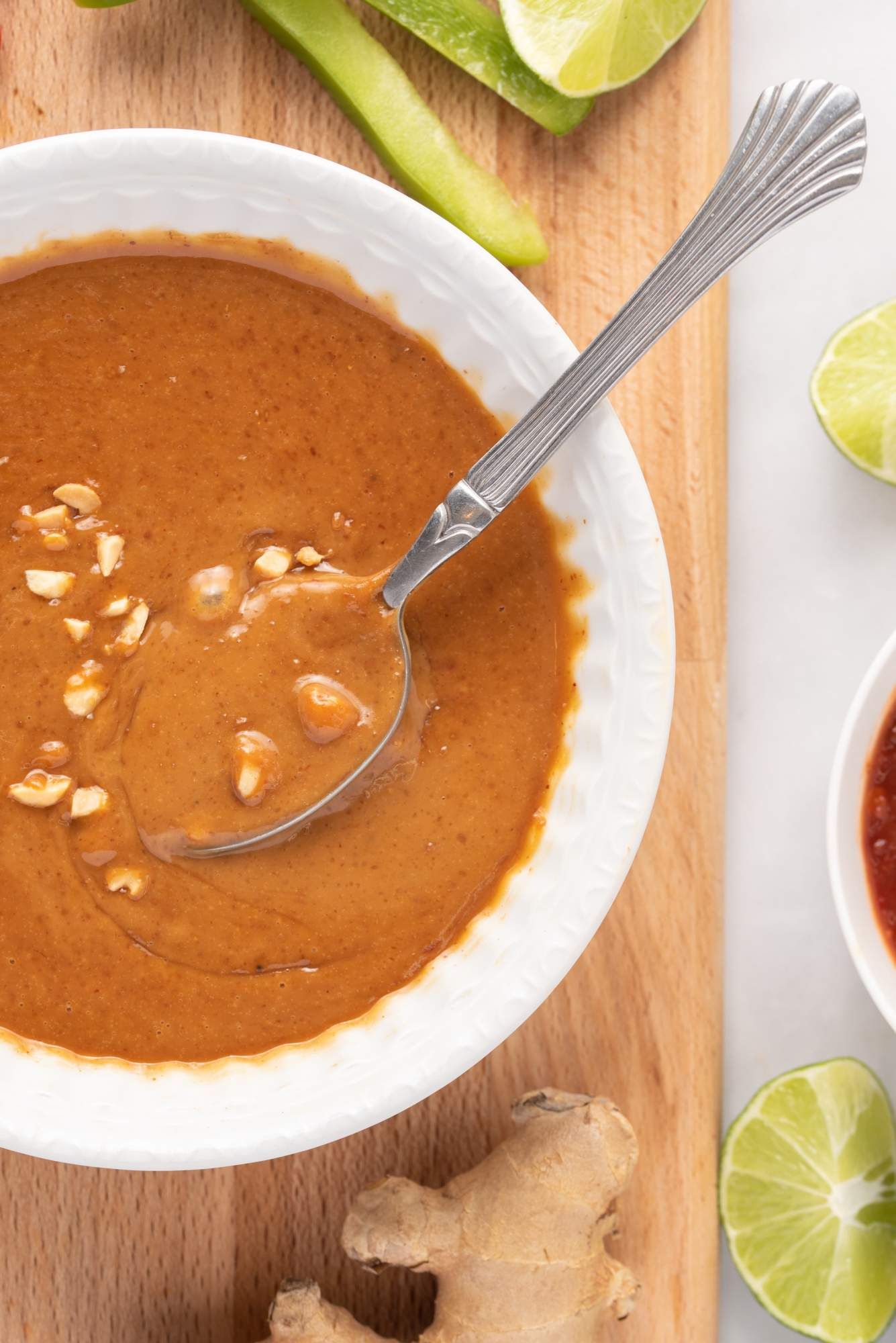 Homemade Asian peanut sauce in a white bowl with crushed peanuts on top and a spoon