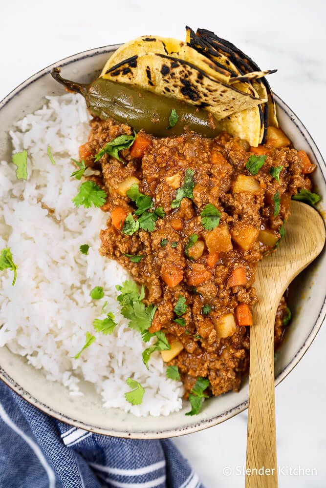 Mexican picadillo in a bowl with corn tortillas, white rice, a jalapeno, and cilantro.