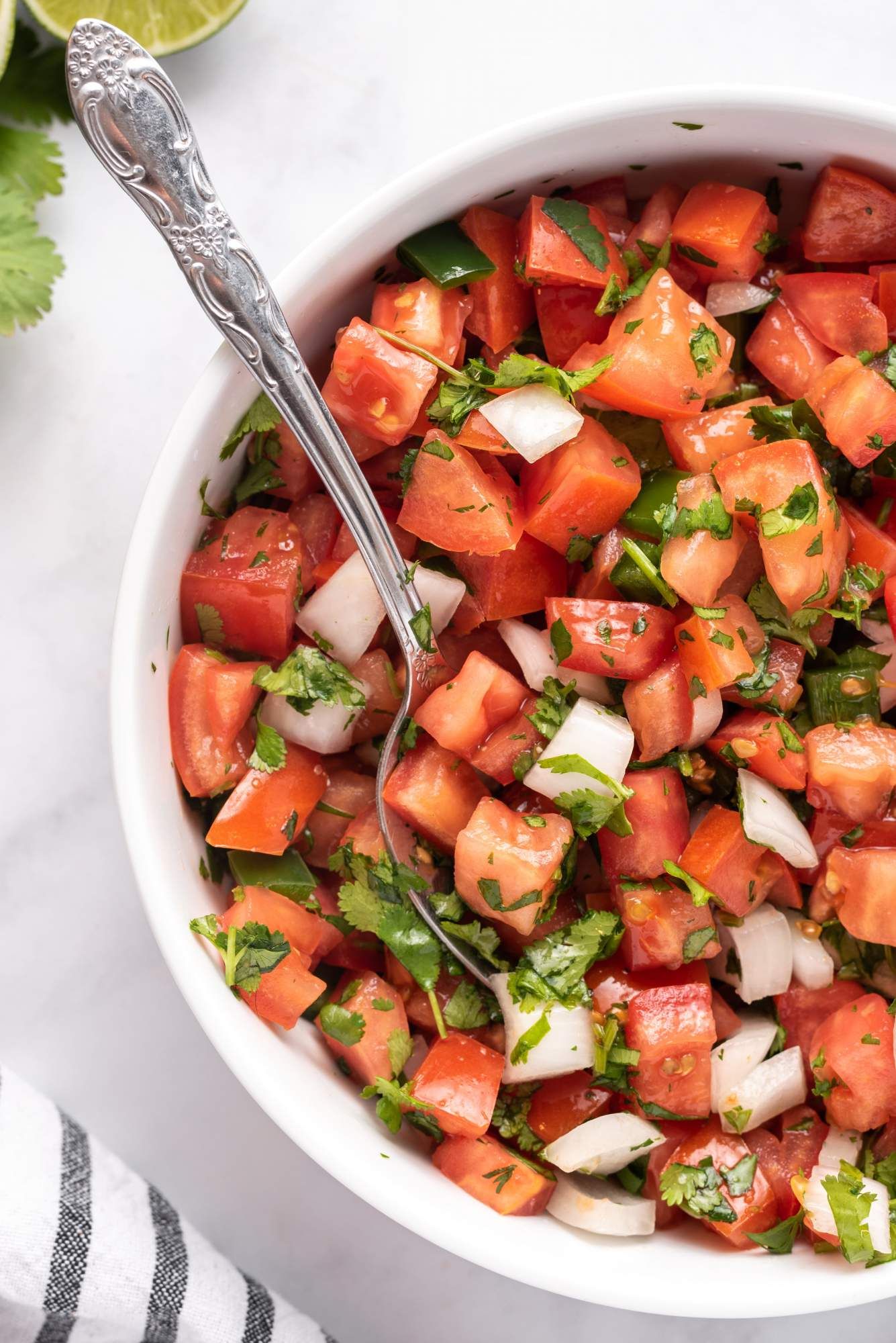 Mexican salsa fresca made with tomatoes, onions, jalapenos, cilantro, and lime juice in a bowl with a spoon.