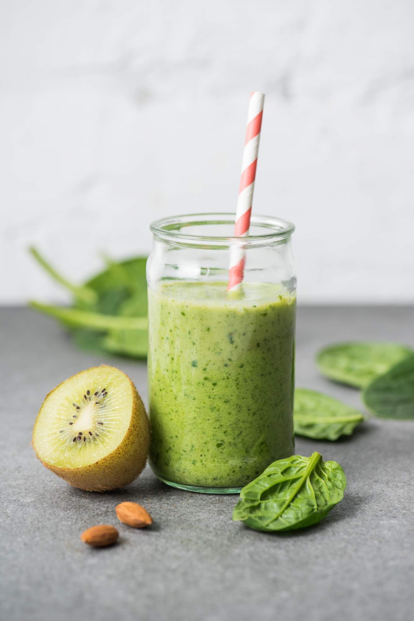 Cucumber smoothie with pineapple, spinach, banana, and coconut water blended in a glass with spinach on the side.