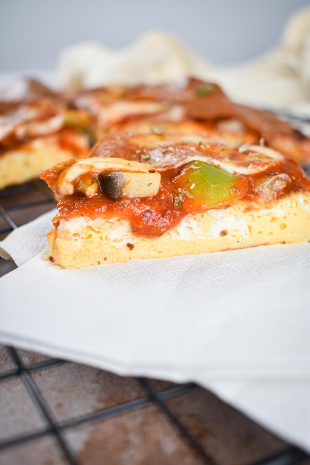 Piza frittata with a layer of eggs, tomato sauce, pizza toppings, and mozzarella cheese on a napkin.