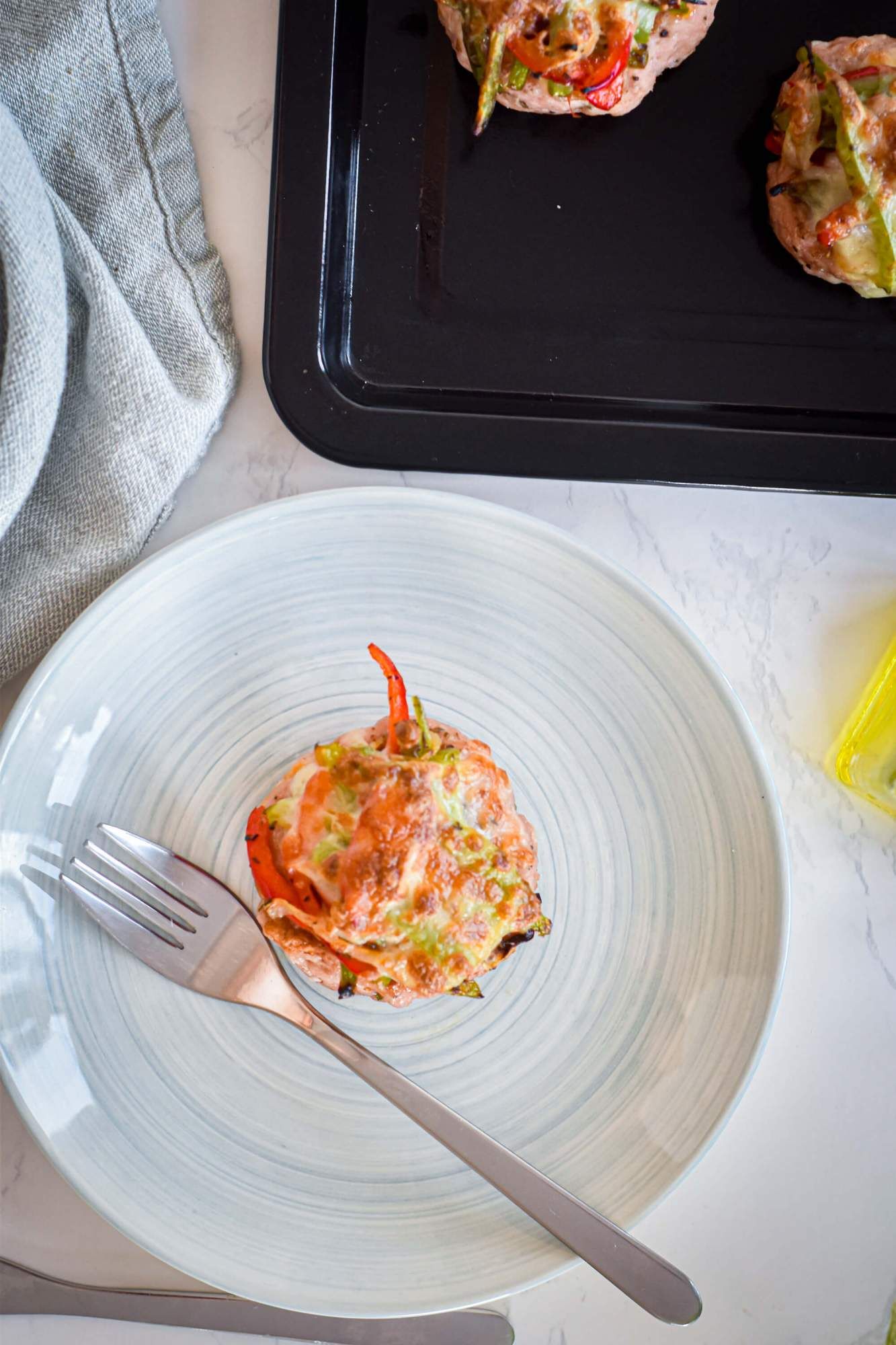 Burgers made with turkey, peppers, onions, and melted cheese on a plate with a blue napkin.