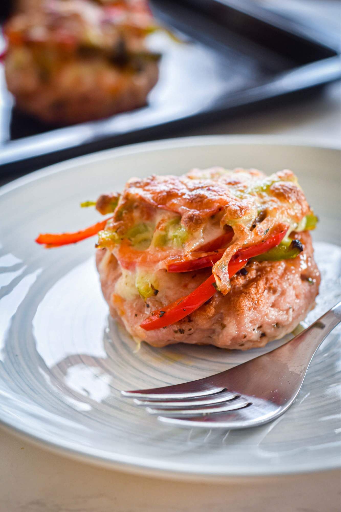 Turkey burgers with spaghetti sauce, peppers, onions, and melted cheese on a plate with a baking sheet.